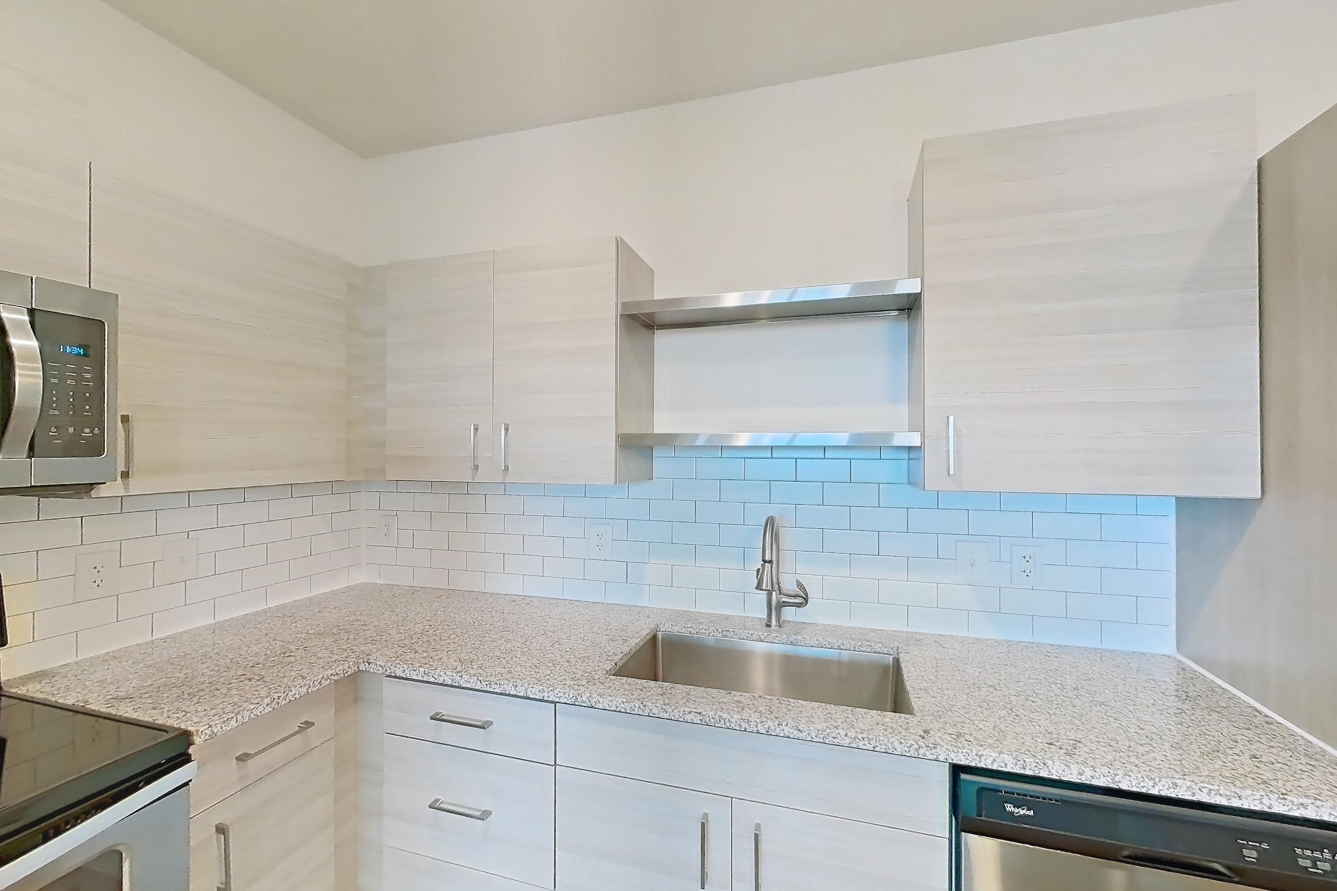 Kitchen with dishwasher, electric range, light countertops, light stone countertops, light wood-finish flooring, oven/range, refrigerator, and stainless steel appliances, Apartment 104-304 at Domain
