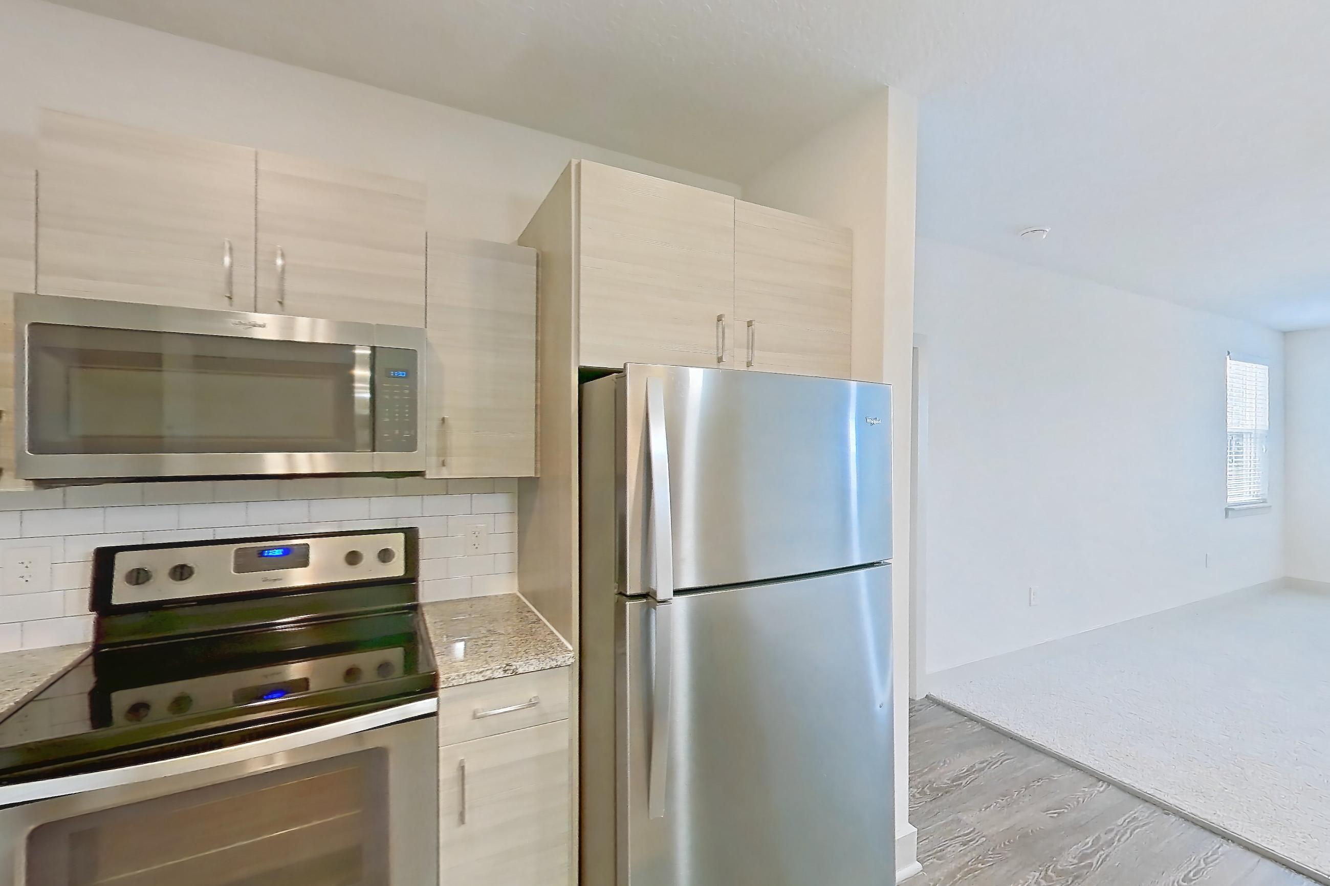 Kitchen with electric range, light countertops, light stone countertops, light wood-finish flooring, microwave, oven/range, refrigerator, and stainless steel appliances, Apartment 144-202 at Domain