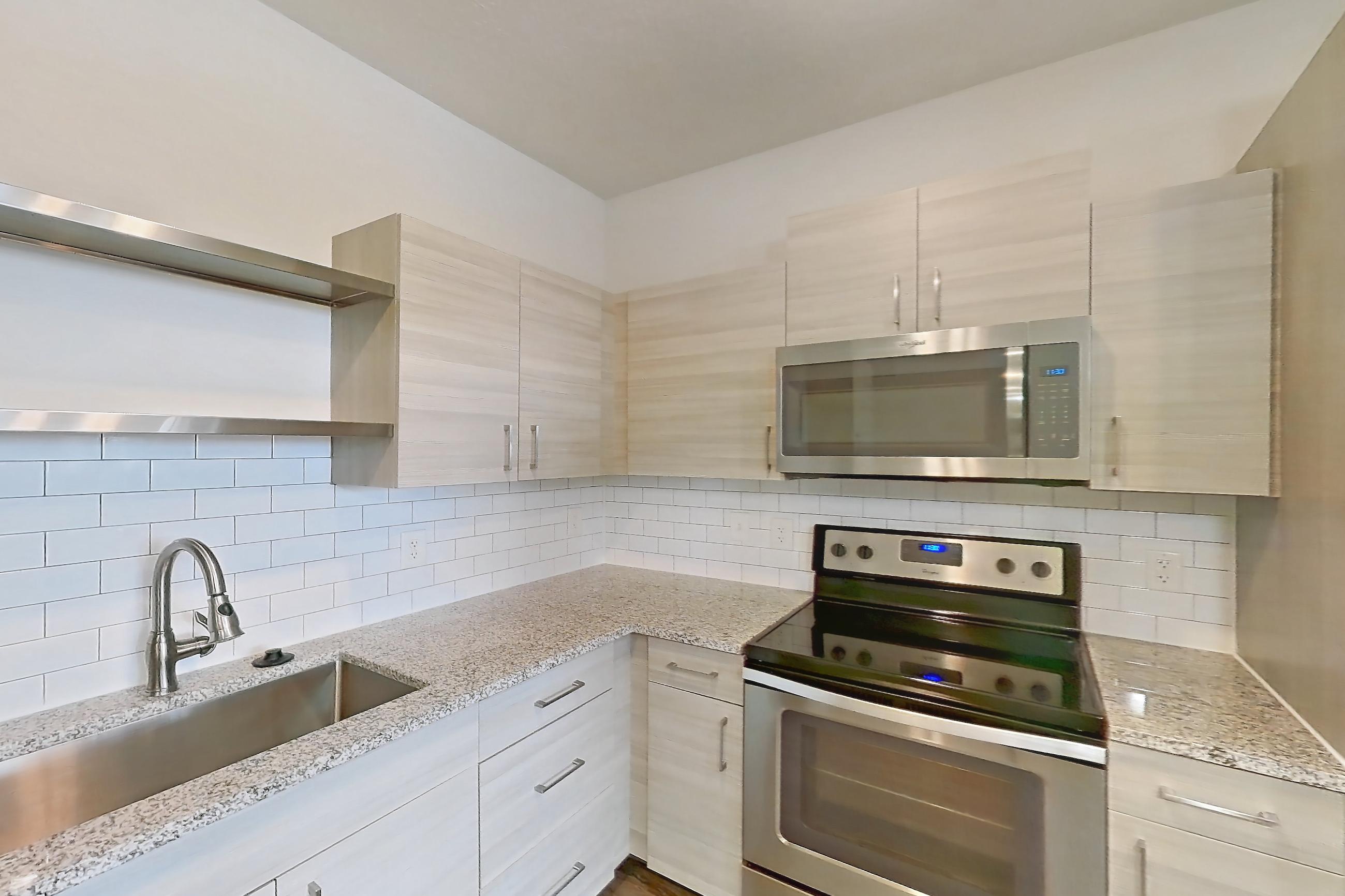 Kitchen with electric range, light countertops, light stone countertops, light wood-finish flooring, microwave, oven/range, refrigerator, and stainless steel appliances, Apartment 144-202 at Domain