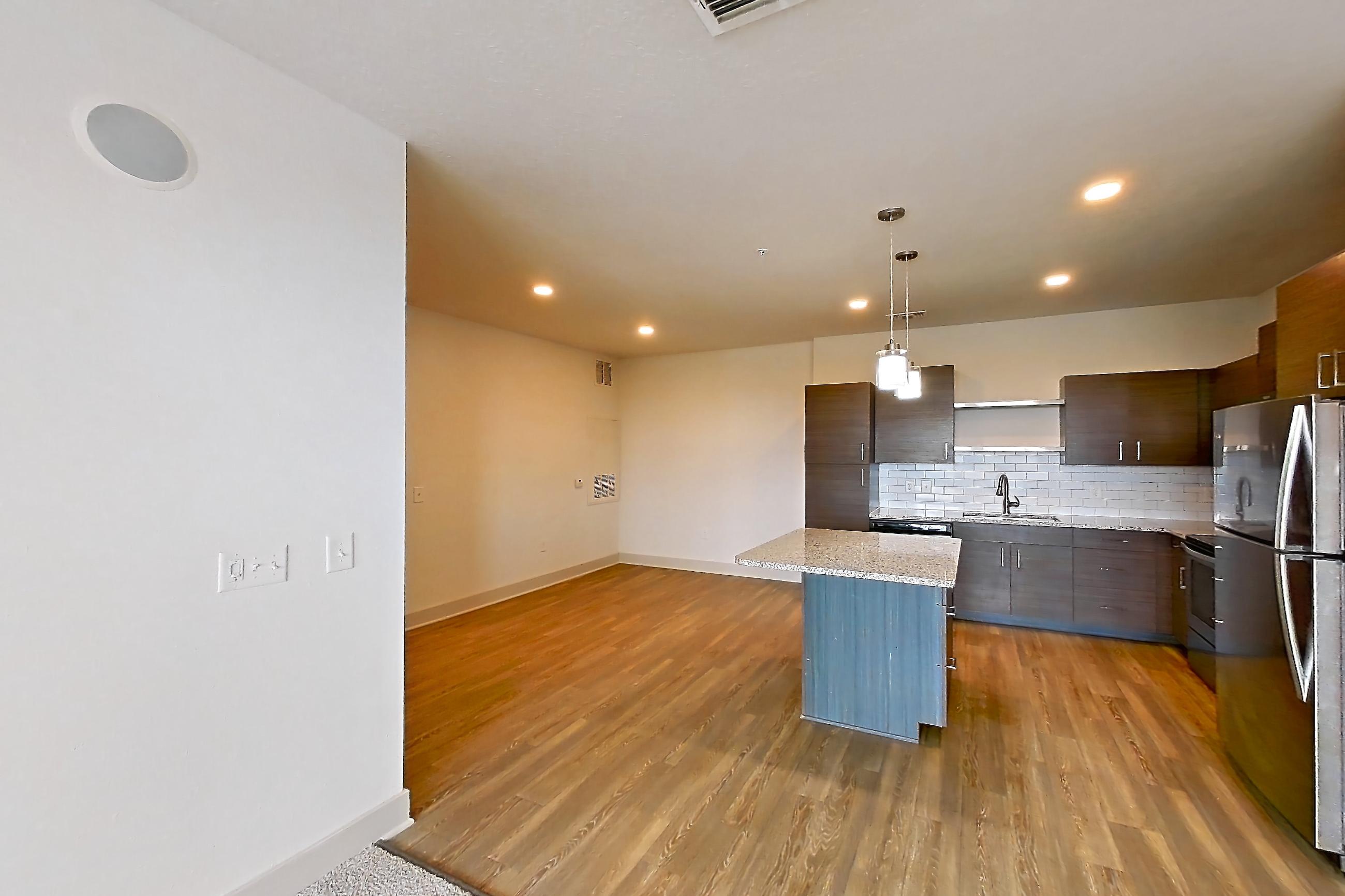 Living room with black appliances, dark wood-finish flooring, dishwasher, and light stone countertops, Apartment 148-302 at Domain