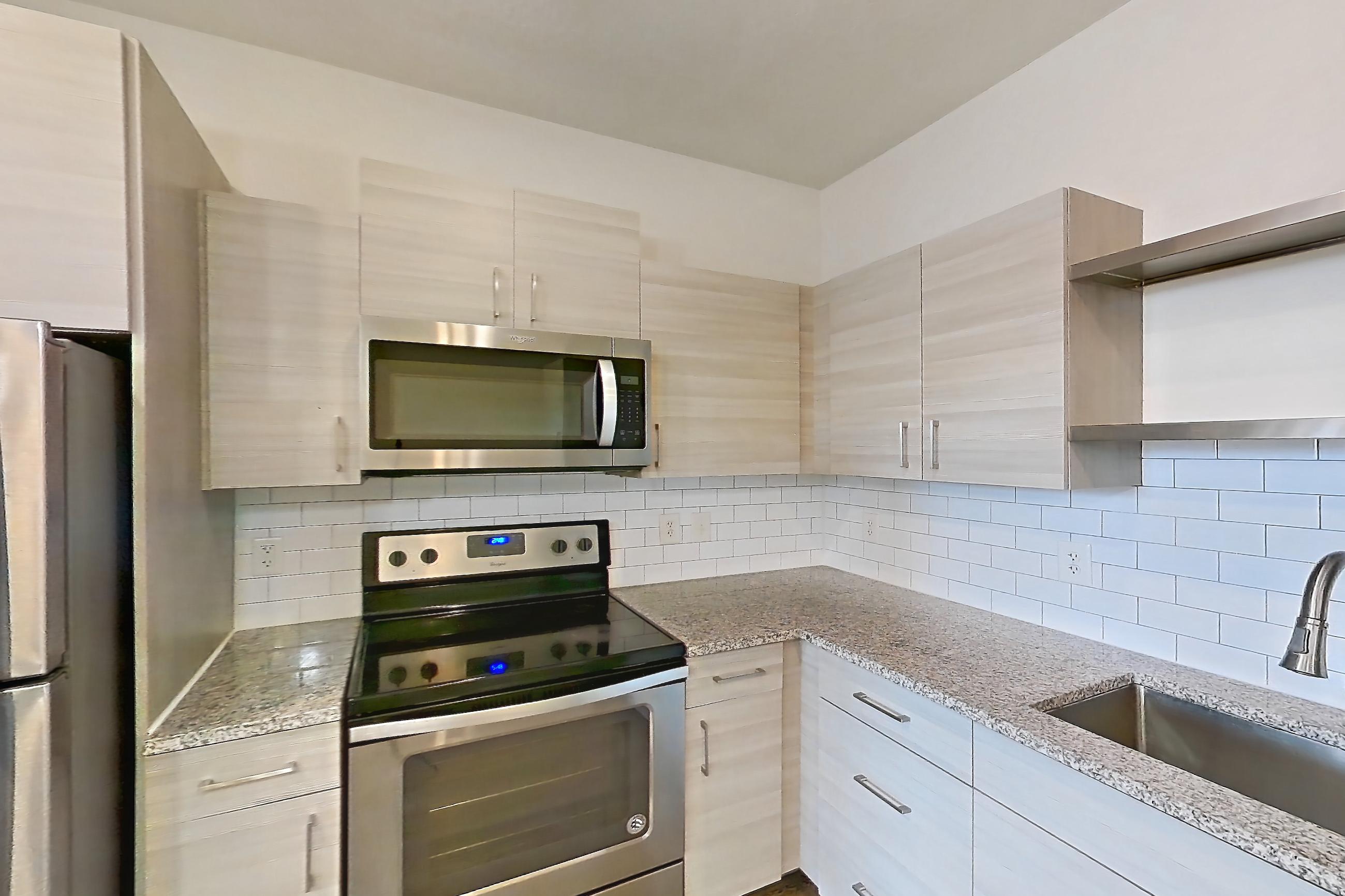 Kitchen with dark wood-finish flooring, dishwasher, electric range, light countertops, light stone countertops, microwave, oven/range, refrigerator, and stainless steel appliances, Apartment 154-204 at Domain