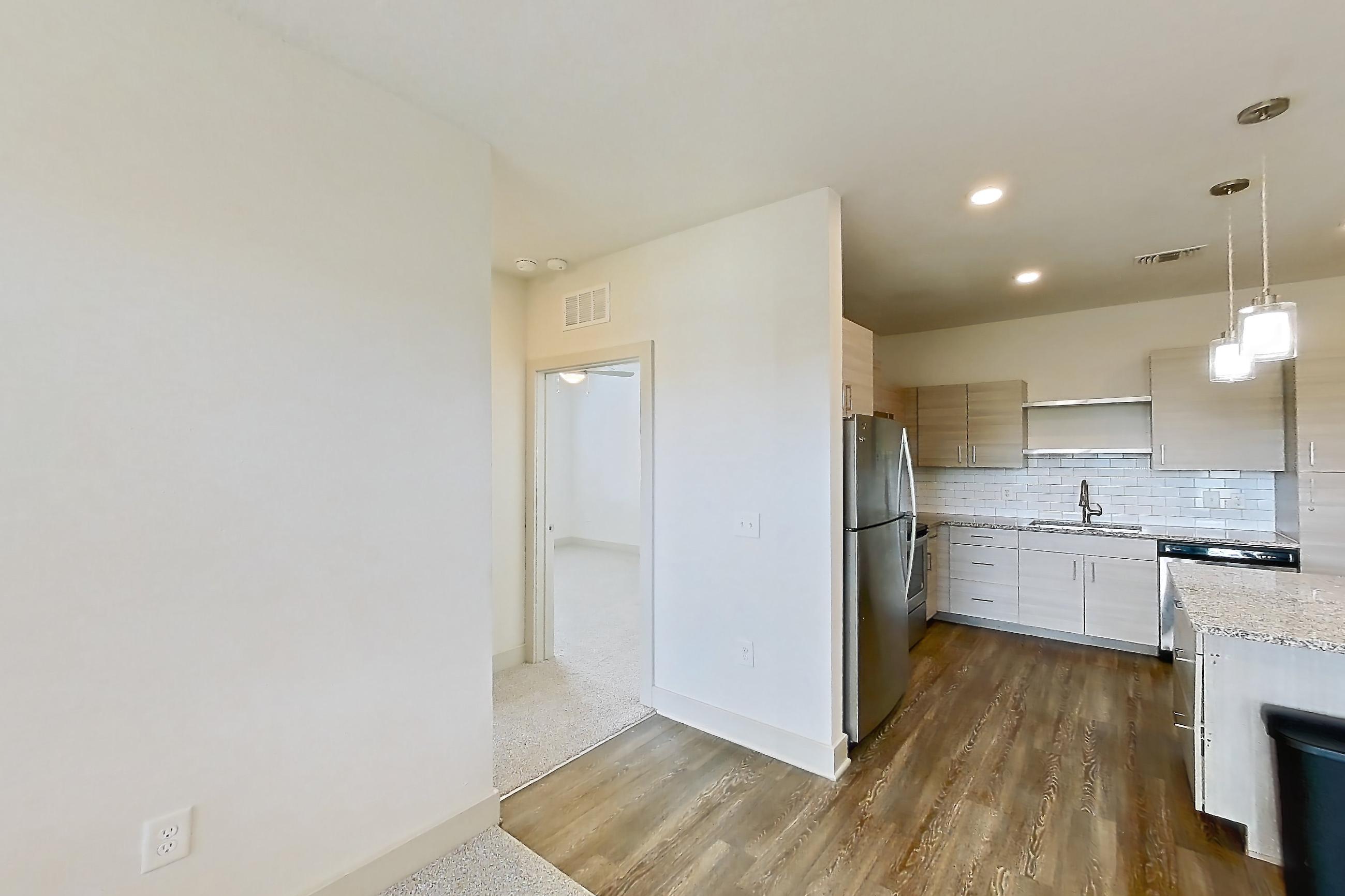 Living room with dark wood-finish flooring, light carpet, light stone countertops, refrigerator, and stainless steel appliances, Apartment 154-204 at Domain