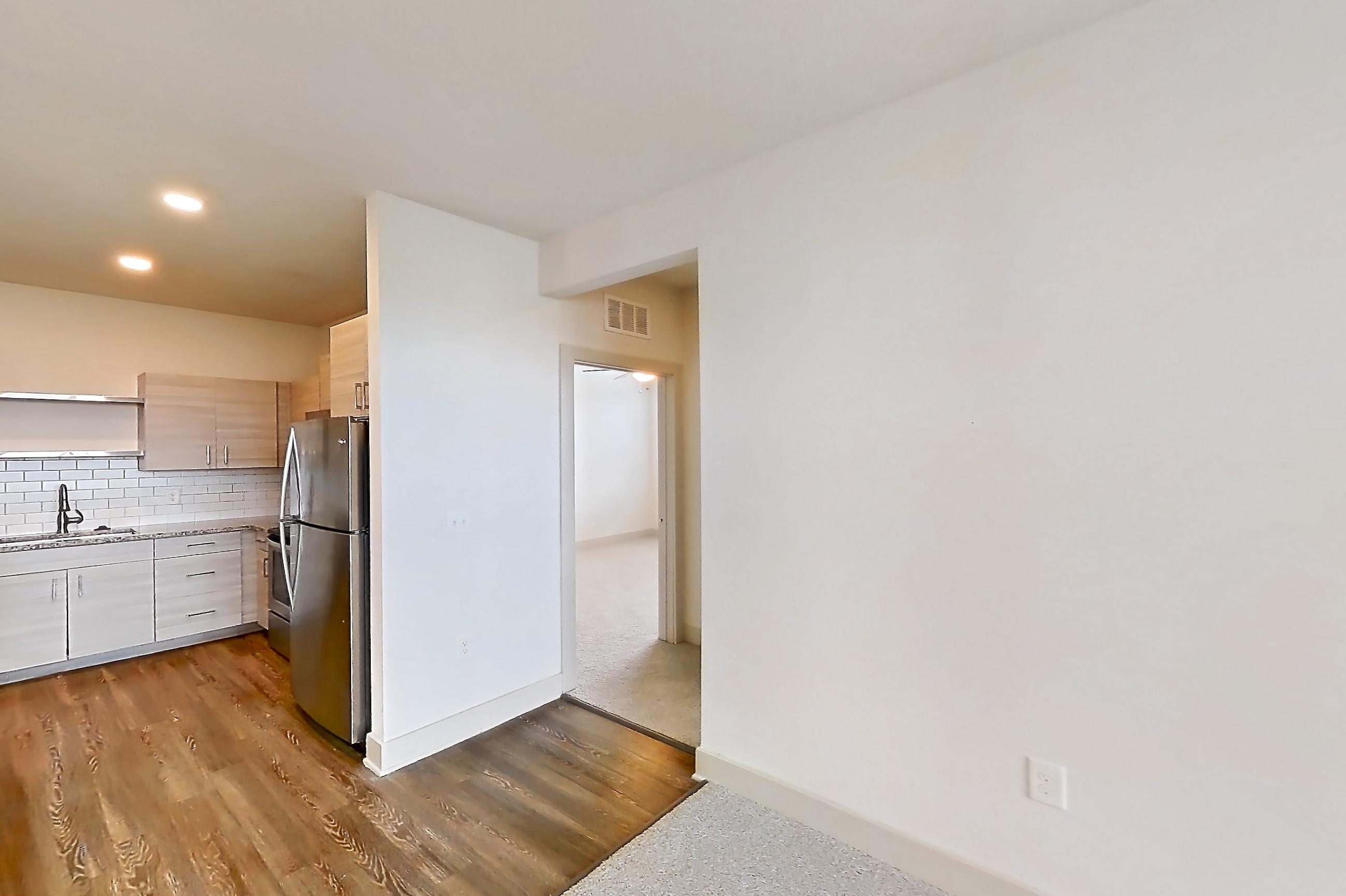 Living room with dark wood-finish flooring, light stone countertops, refrigerator, and stainless steel appliances, Apartment 116-302 at Domain