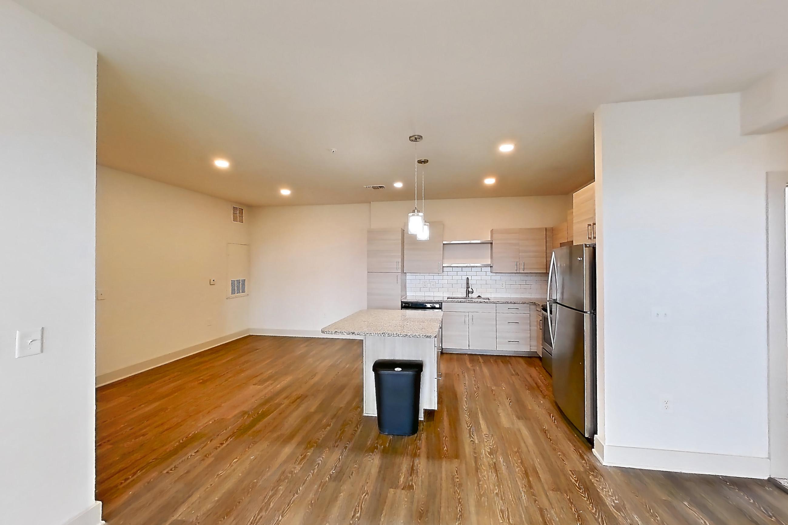 Living room with dark wood-finish flooring, light stone countertops, refrigerator, and stainless steel appliances, Apartment 116-302 at Domain