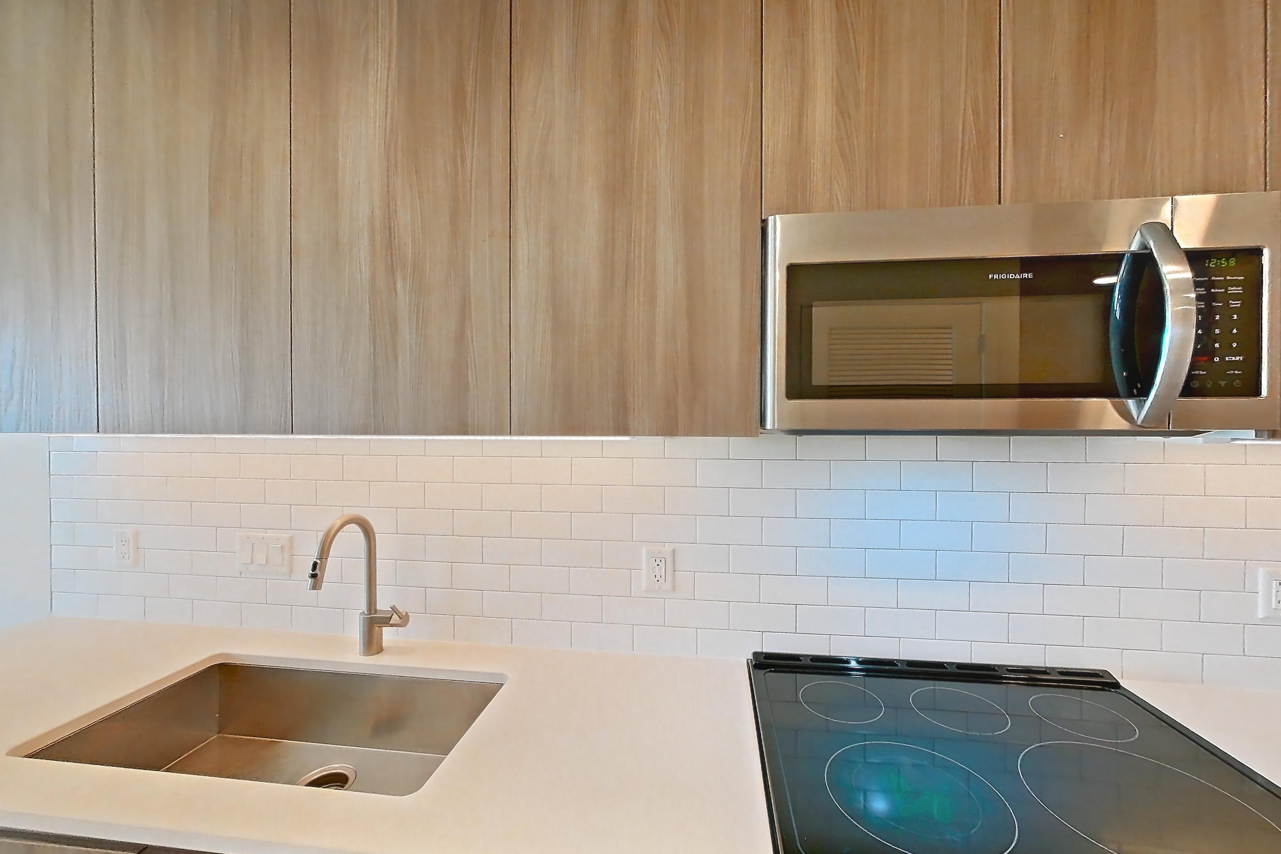 Kitchen with dishwasher, electric range, light countertops, light stone countertops, light wood-finish flooring, microwave, oven/range, refrigerator, and stainless steel appliances, Apartment 2507 at Platform (VA)