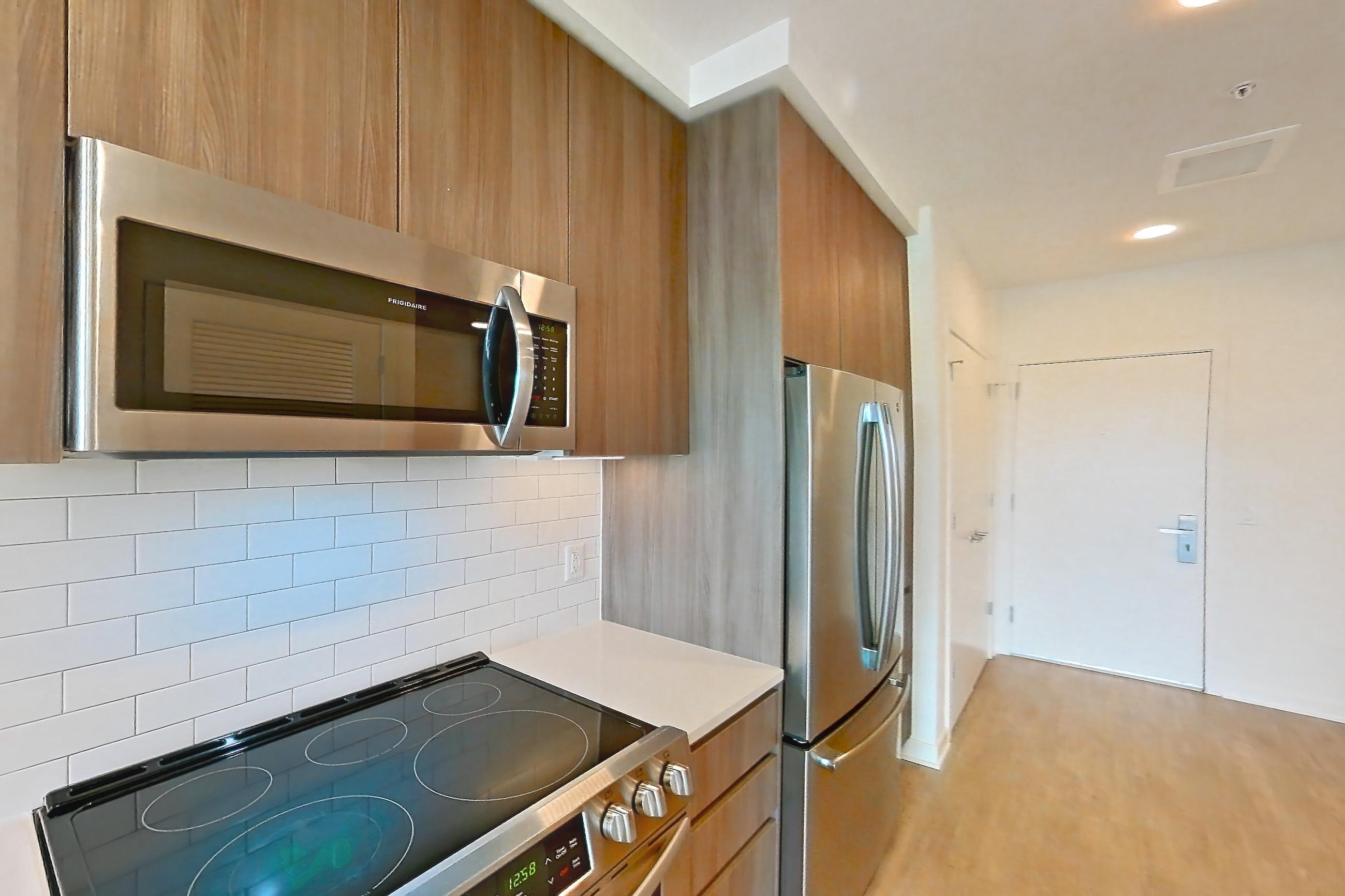 Kitchen with dishwasher, electric range, light countertops, light stone countertops, light wood-finish flooring, microwave, oven/range, refrigerator, and stainless steel appliances, Apartment 2507 at Platform (VA)