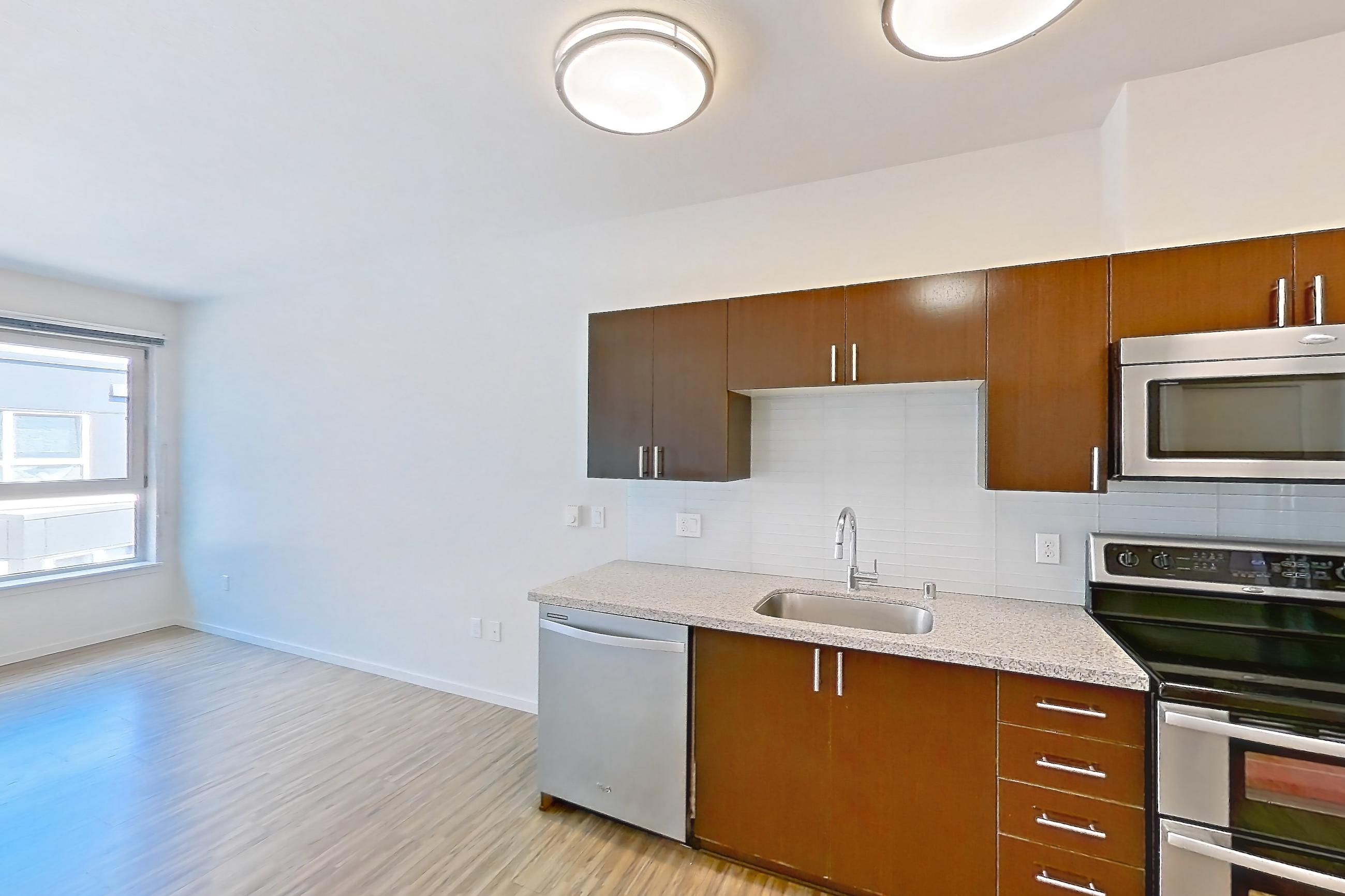 Kitchen with dishwasher, double oven, electric range, light countertops, light stone countertops, light wood-finish flooring, microwave, oven/range, refrigerator, and stainless steel appliances, Unit L708 at Union SLU