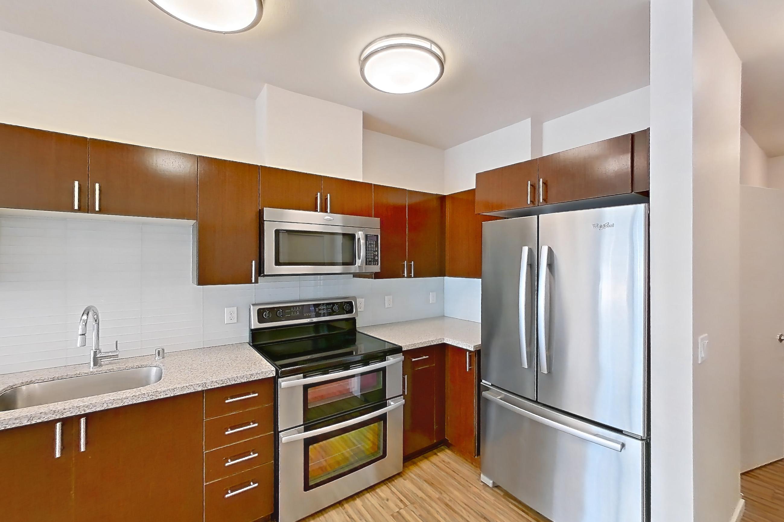 Kitchen with dishwasher, double oven, electric range, light countertops, light stone countertops, light wood-finish flooring, microwave, oven/range, refrigerator, and stainless steel appliances, Unit L708 at Union SLU