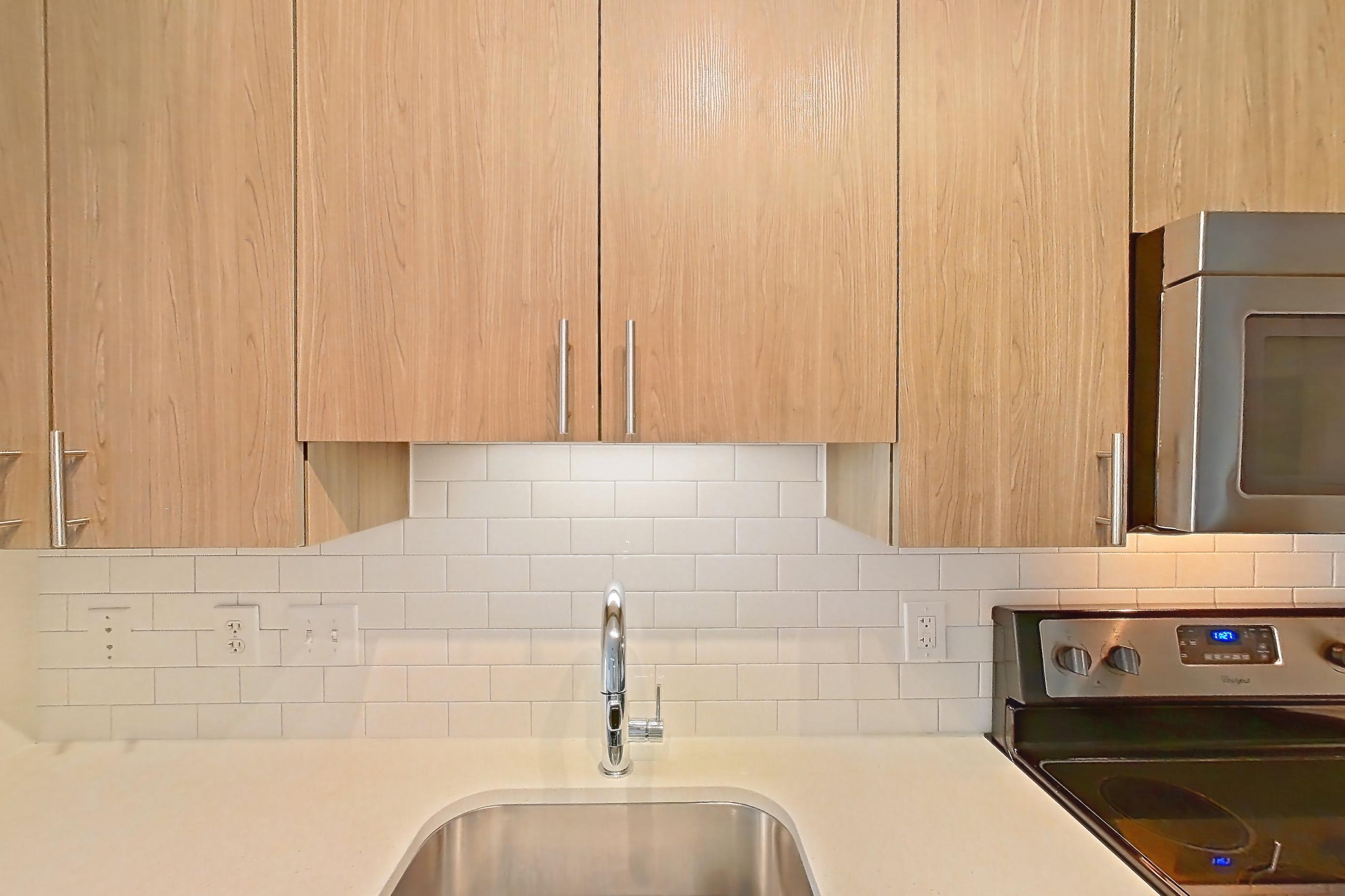 Kitchen with dark wood-finish flooring, dishwasher, electric range, light countertops, light stone countertops, oven/range, refrigerator, and stainless steel appliances, Apartment 1-421 at The Parker at Huntington Metro