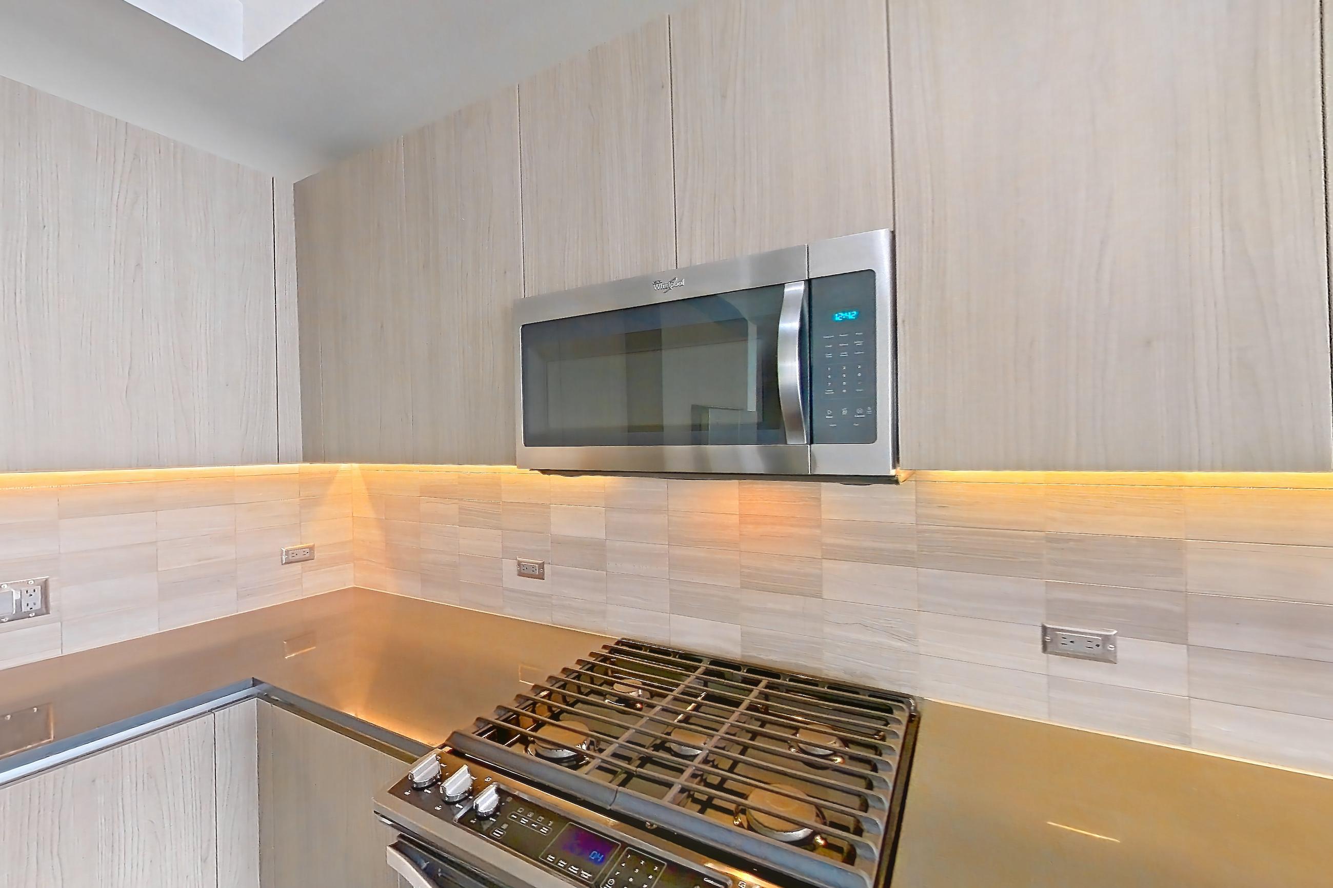 Kitchen with dark wood-finish flooring, gas range, oven/range, refrigerator, stainless steel appliances, and water & ice dispenser, Apartment 1801 at Cortland Museum District