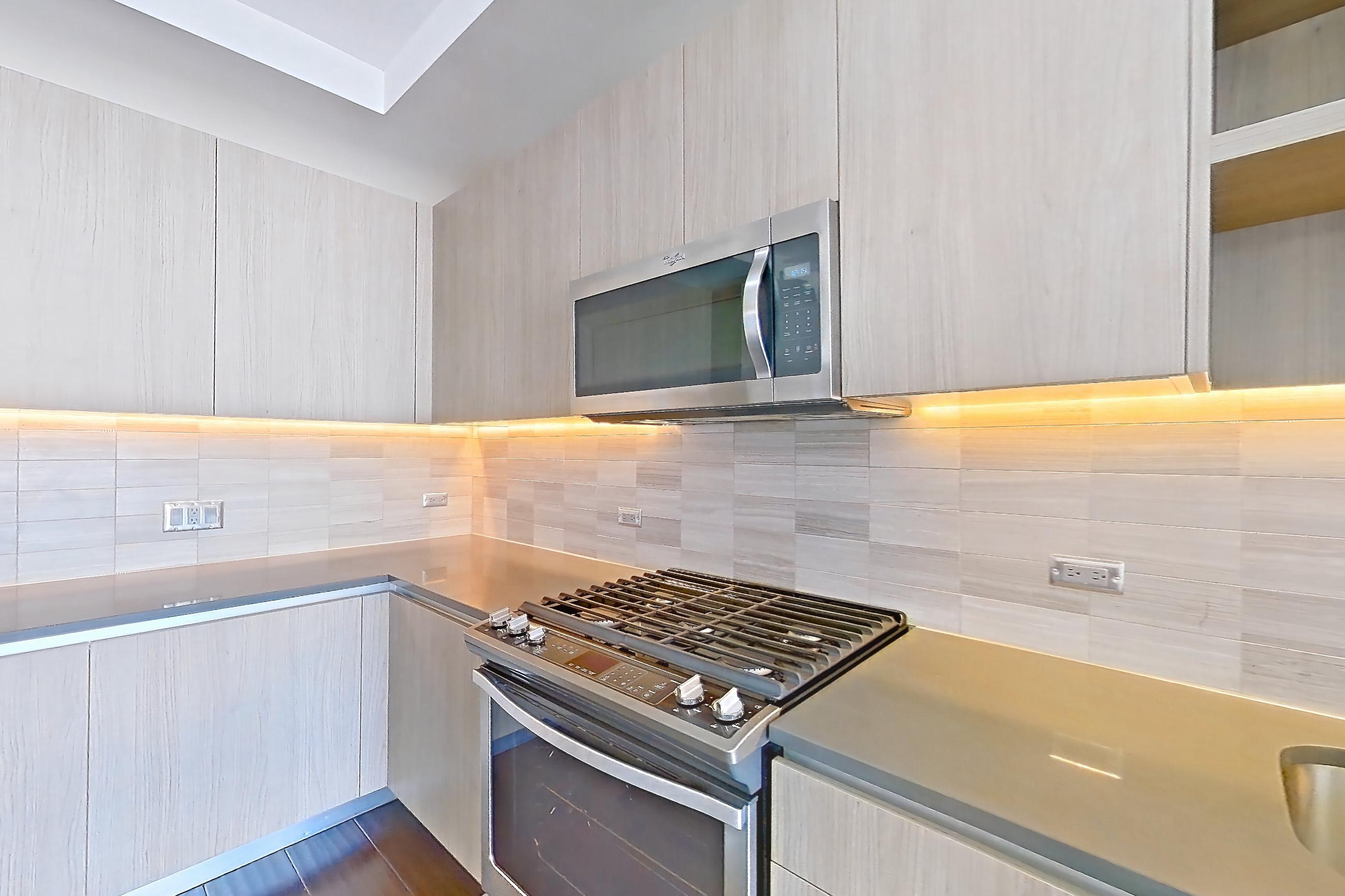 Kitchen with dark wood-finish flooring, gas range, microwave, oven/range, refrigerator, stainless steel appliances, water & ice dispenser, and wood-finish flooring, Apartment 1001 at Cortland Museum District