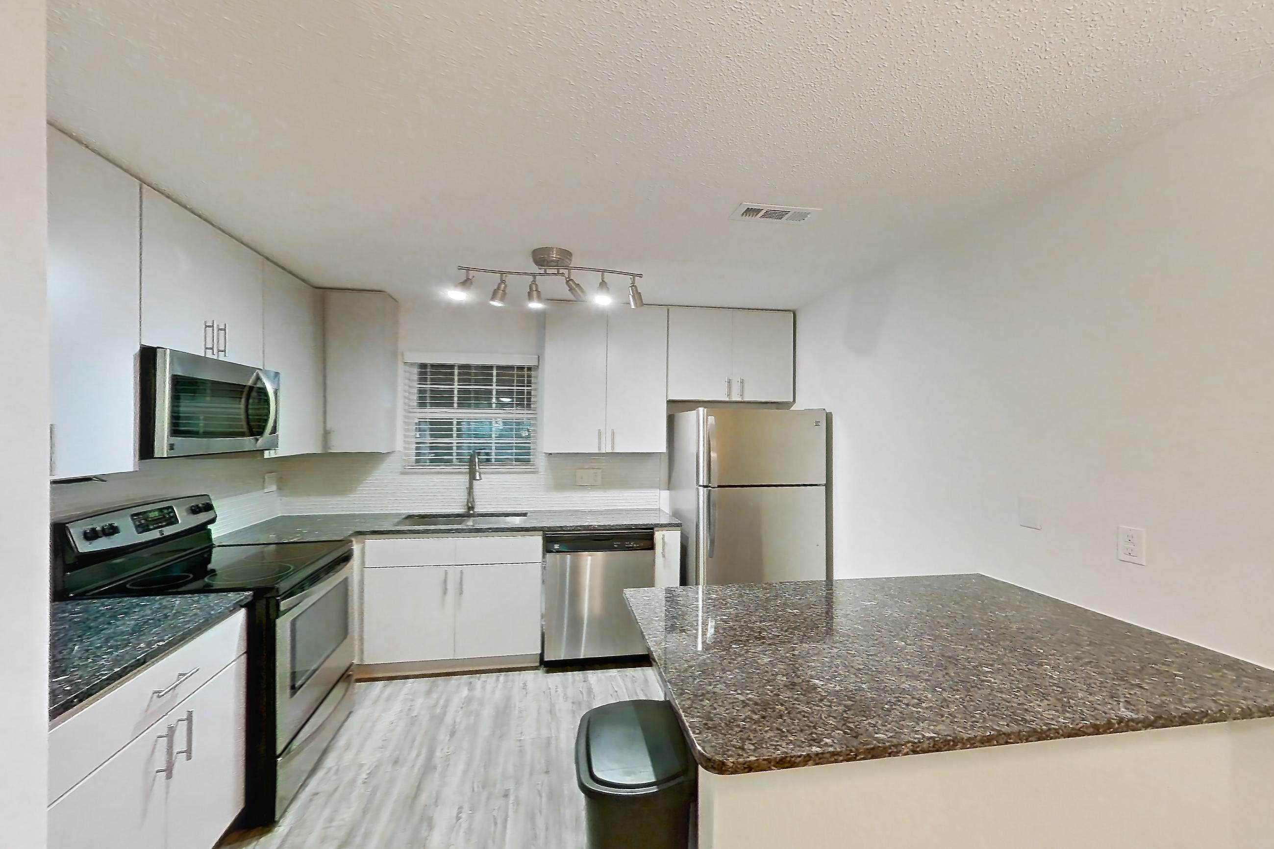 Dining room with dark stone countertops, dark wood-finish flooring, dishwasher, electric range, fireplace, light countertops, light wood-finish flooring, microwave, oven/range, refrigerator, stainless steel appliances, tile fireplace, and white appliances, Apartment 3 at Cortland Cotswold