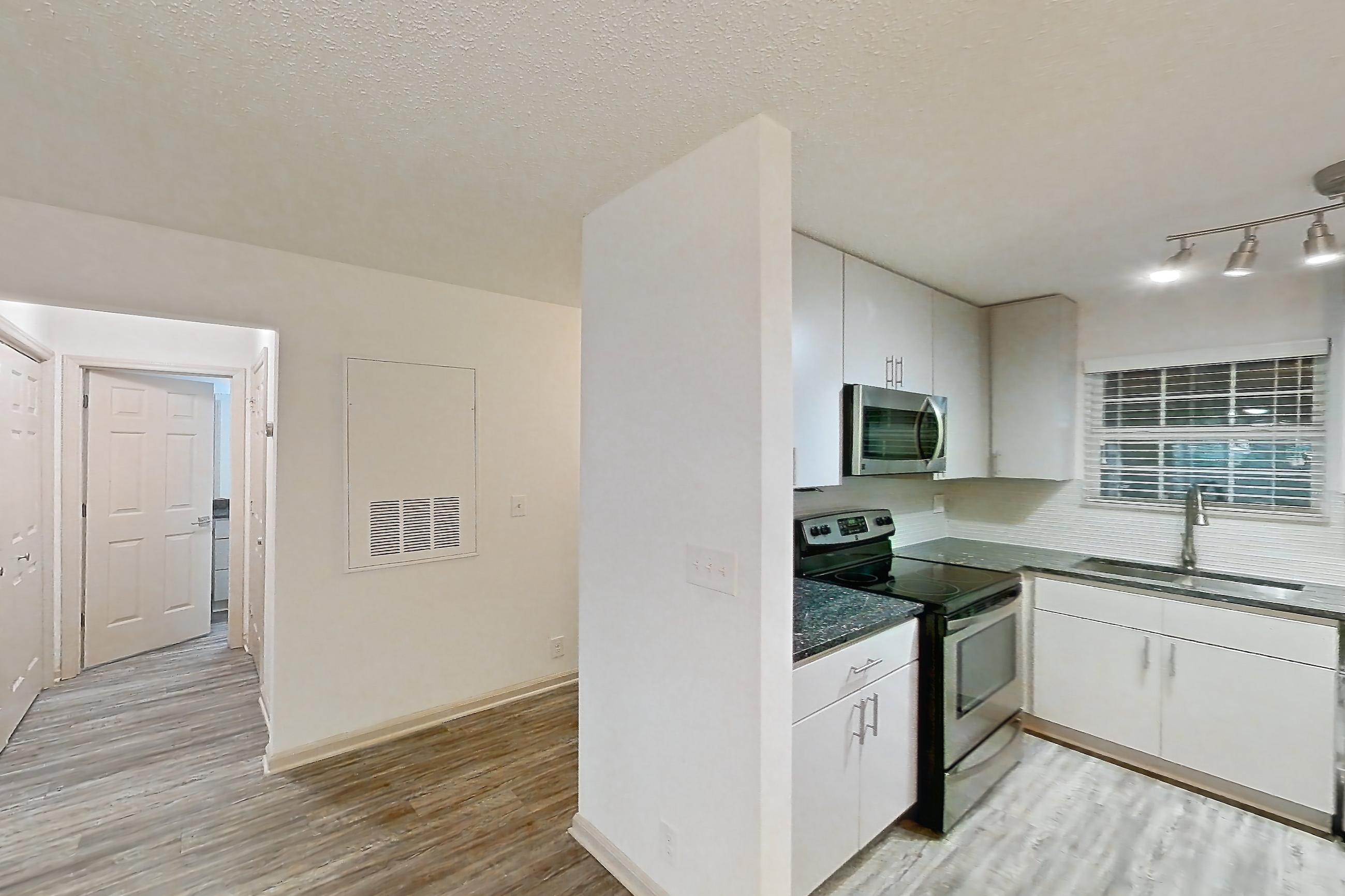 Dining room with dark stone countertops, dark wood-finish flooring, dishwasher, electric range, fireplace, light countertops, light wood-finish flooring, microwave, oven/range, refrigerator, stainless steel appliances, tile fireplace, and white appliances, Apartment 3 at Cortland Cotswold