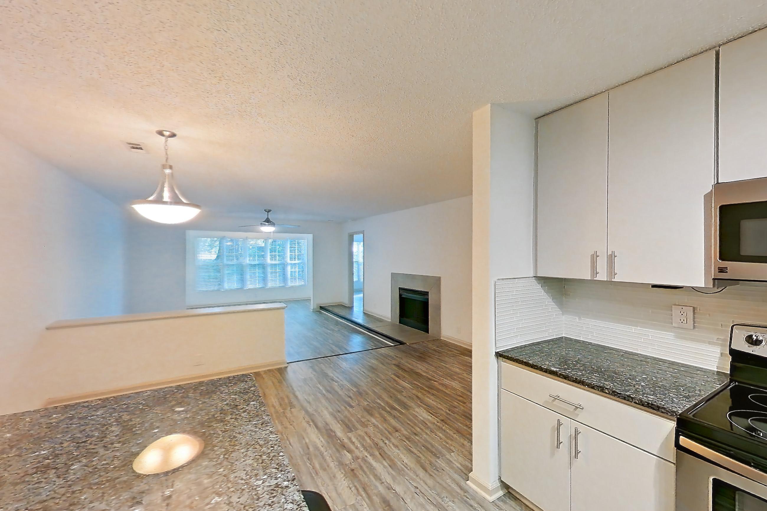 Kitchen with dark stone countertops, dishwasher, electric range, fireplace, light countertops, light wood-finish flooring, microwave, oven/range, refrigerator, and stainless steel appliances, Apartment 3 at Cortland Cotswold