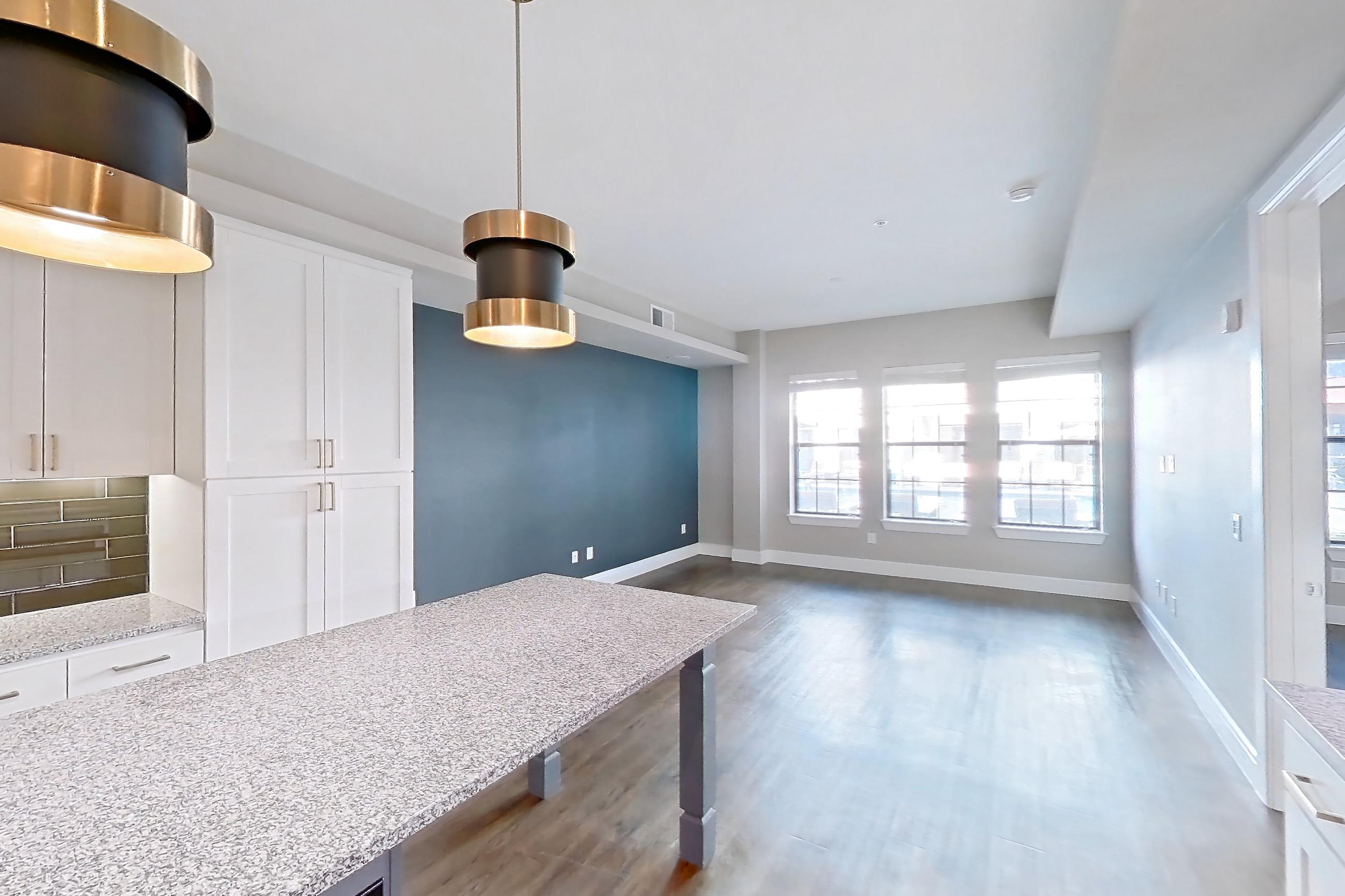 Kitchen with dark wood-finish flooring, dishwasher, gas range, light countertops, light stone countertops, oven/range, refrigerator, stainless steel appliances, and water & ice dispenser, Apartment 105 at Cortland Biltmore
