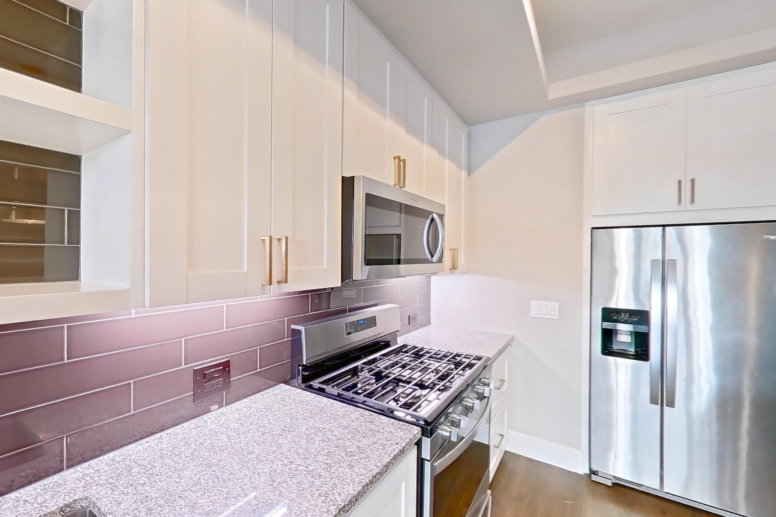 Kitchen with dark wood-finish flooring, dishwasher, gas range, light countertops, light stone countertops, oven/range, refrigerator, stainless steel appliances, and water & ice dispenser, Apartment 105 at Cortland Biltmore