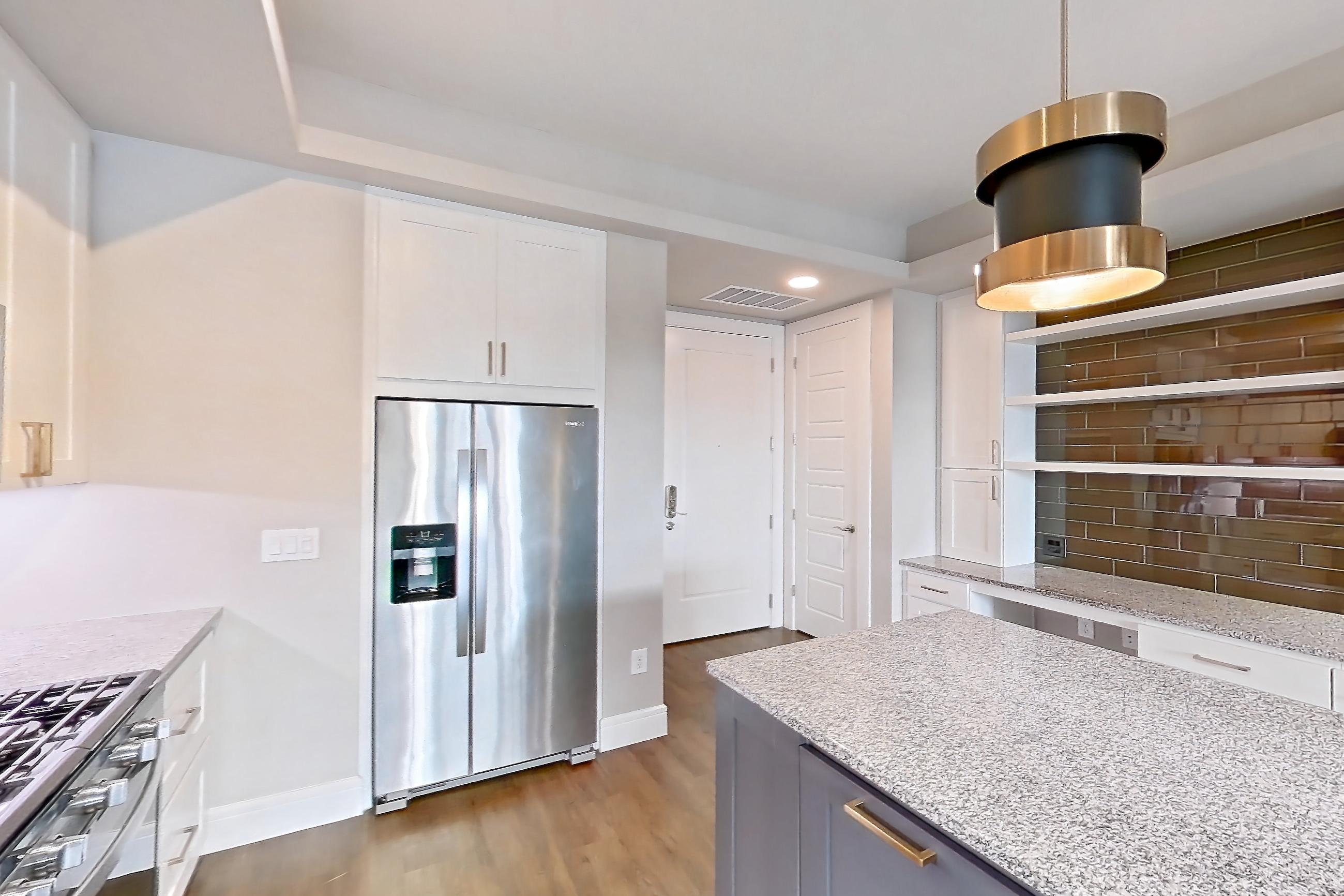 Kitchen with dark wood-finish flooring, dishwasher, gas range, light countertops, light stone countertops, oven/range, refrigerator, stainless steel appliances, and water & ice dispenser, Apartment 105 at Cortland Biltmore