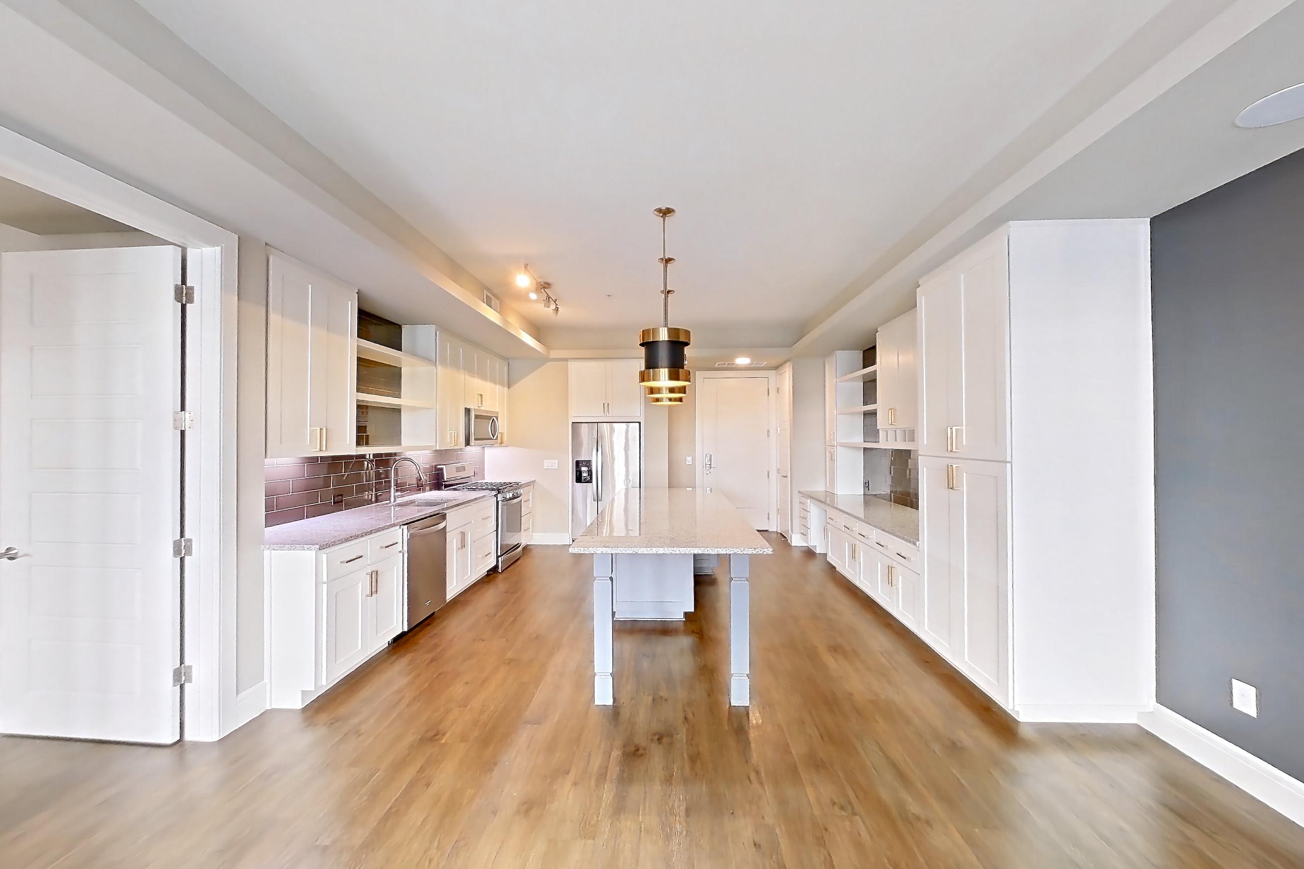 Living room with dark wood-finish flooring, dishwasher, gas range, light stone countertops, oven/range, refrigerator, stainless steel appliances, and water & ice dispenser, Apartment 105 at Cortland Biltmore