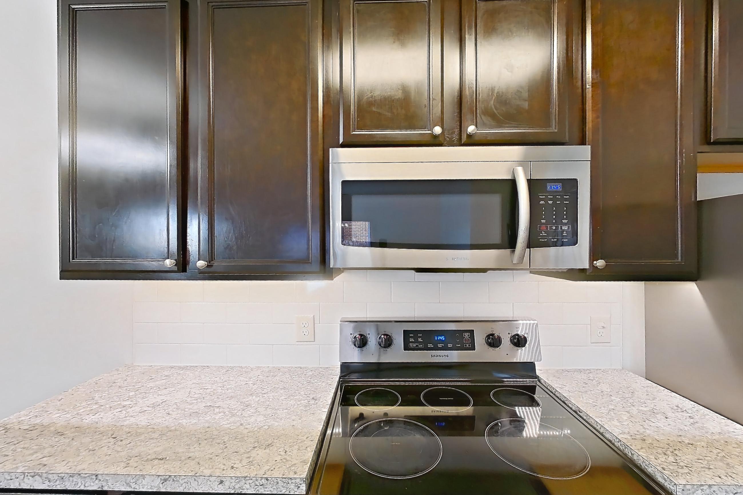 Kitchen with dishwasher, electric range, light countertops, light stone countertops, light wood-finish flooring, microwave, oven/range, refrigerator, and stainless steel appliances, Apartment 108-4839 at Cortland Hilliard