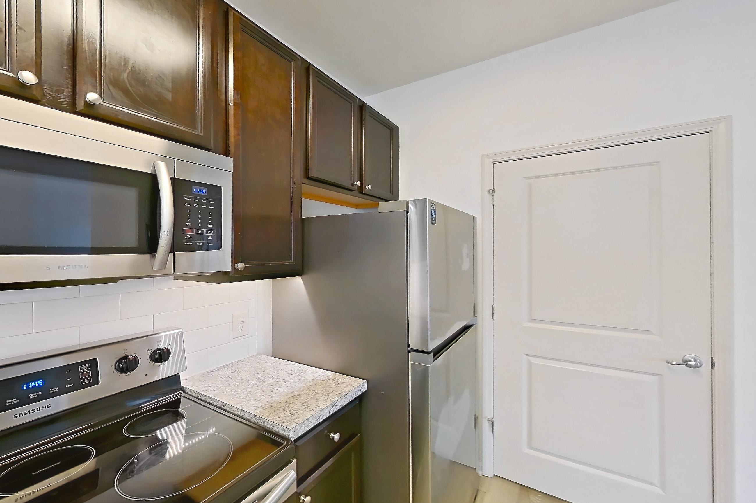Kitchen with dishwasher, electric range, light countertops, light stone countertops, light wood-finish flooring, microwave, oven/range, refrigerator, and stainless steel appliances, Apartment 108-4839 at Cortland Hilliard