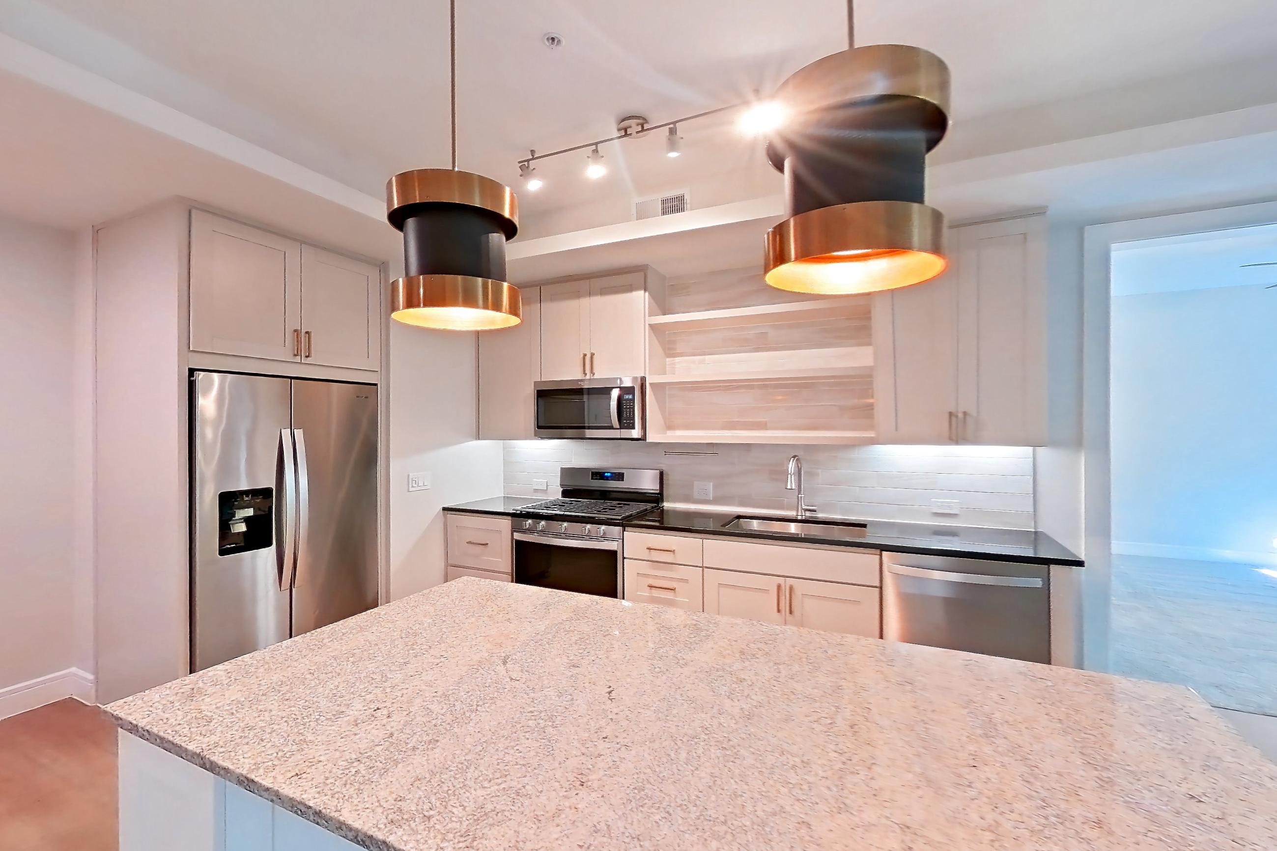 Dining room with dark stone countertops, dishwasher, gas range, light countertops, light stone countertops, light wood-finish flooring, oven/range, refrigerator, stainless steel appliances, and water & ice dispenser, Apartment 234 at Cortland Biltmore
