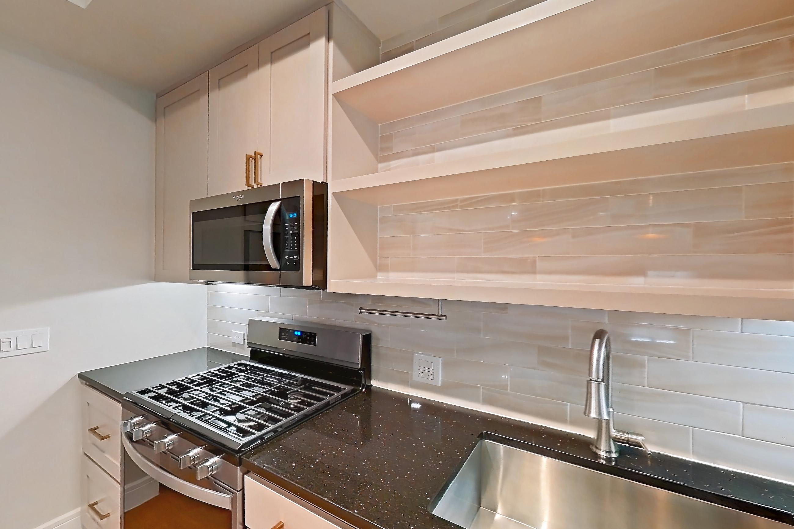 Kitchen with dark stone countertops, dishwasher, gas range, light countertops, light stone countertops, light wood-finish flooring, oven/range, and stainless steel appliances, Apartment 234 at Cortland Biltmore