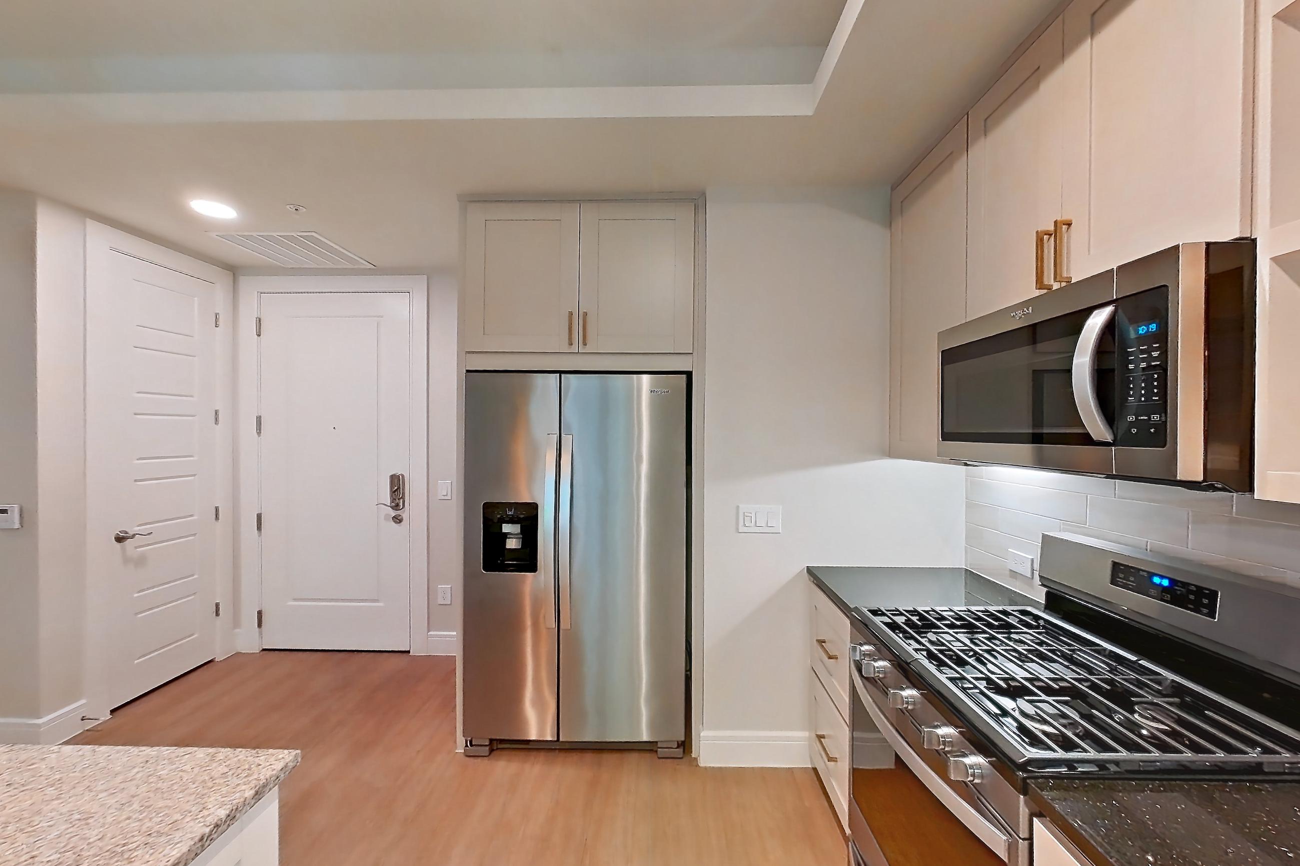 Kitchen with dark stone countertops, dishwasher, gas range, light countertops, light stone countertops, light wood-finish flooring, oven/range, and stainless steel appliances, Apartment 234 at Cortland Biltmore