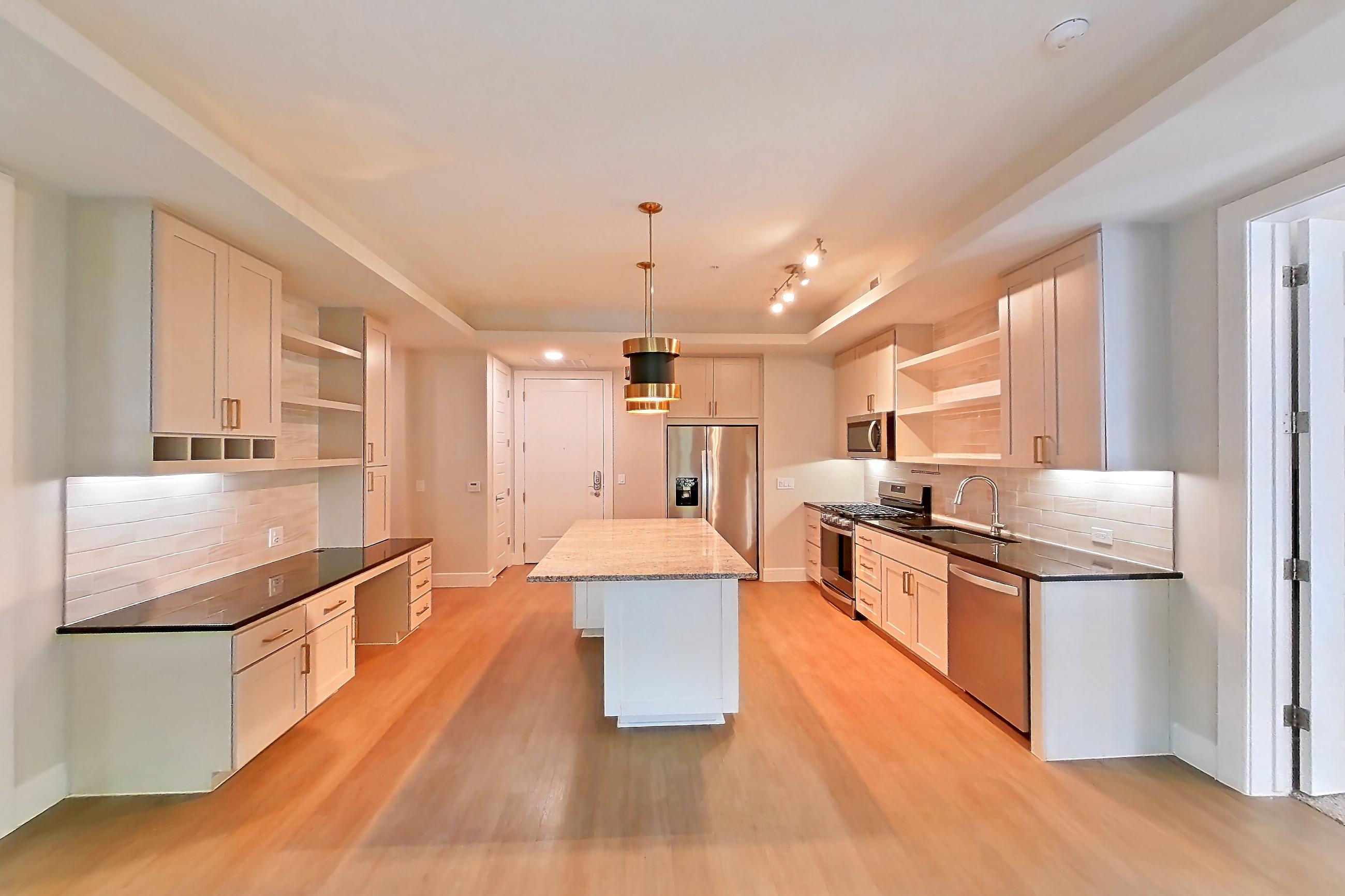 Living room with dark stone countertops, dishwasher, gas range, light countertops, light wood-finish flooring, oven/range, refrigerator, stainless steel appliances, and water & ice dispenser, Apartment 234 at Cortland Biltmore