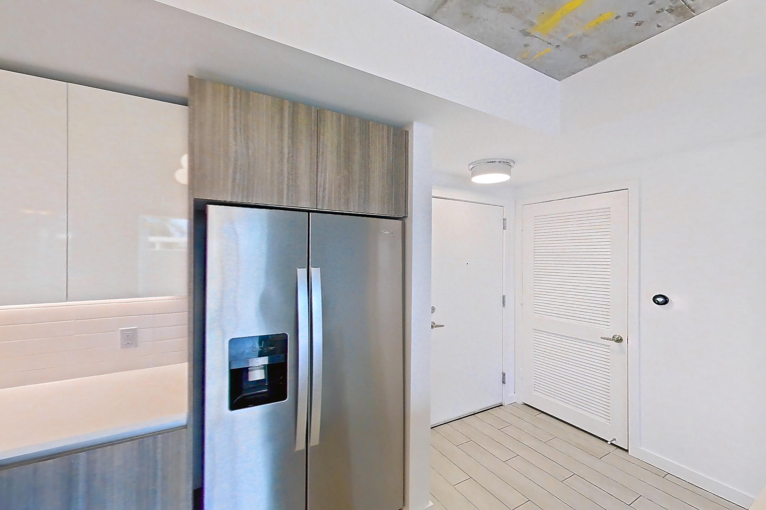 Kitchen with dishwasher, electric range, light countertops, light stone countertops, light tile flooring, light wood-finish flooring, microwave, oven/range, refrigerator, stainless steel appliances, and water & ice dispenser, Apartment 0312 at Cortland Midtown Miami
