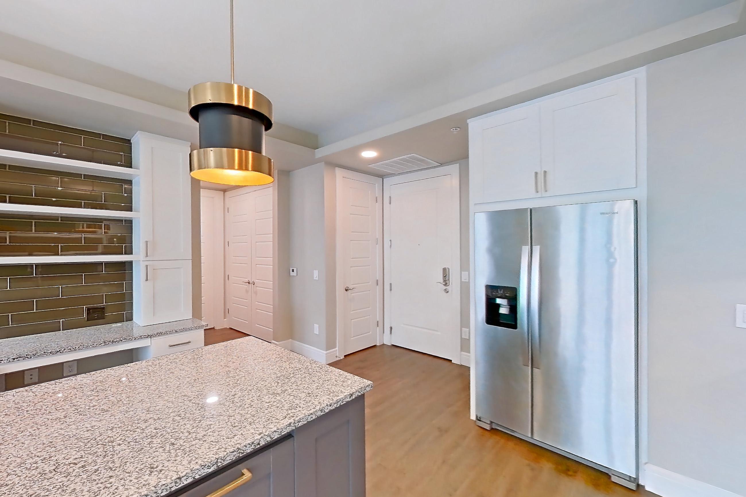 Kitchen with dark wood-finish flooring, dishwasher, gas range, light countertops, light stone countertops, light wood-finish flooring, oven/range, refrigerator, stainless steel appliances, and water & ice dispenser, Apartment 317 at Cortland Biltmore