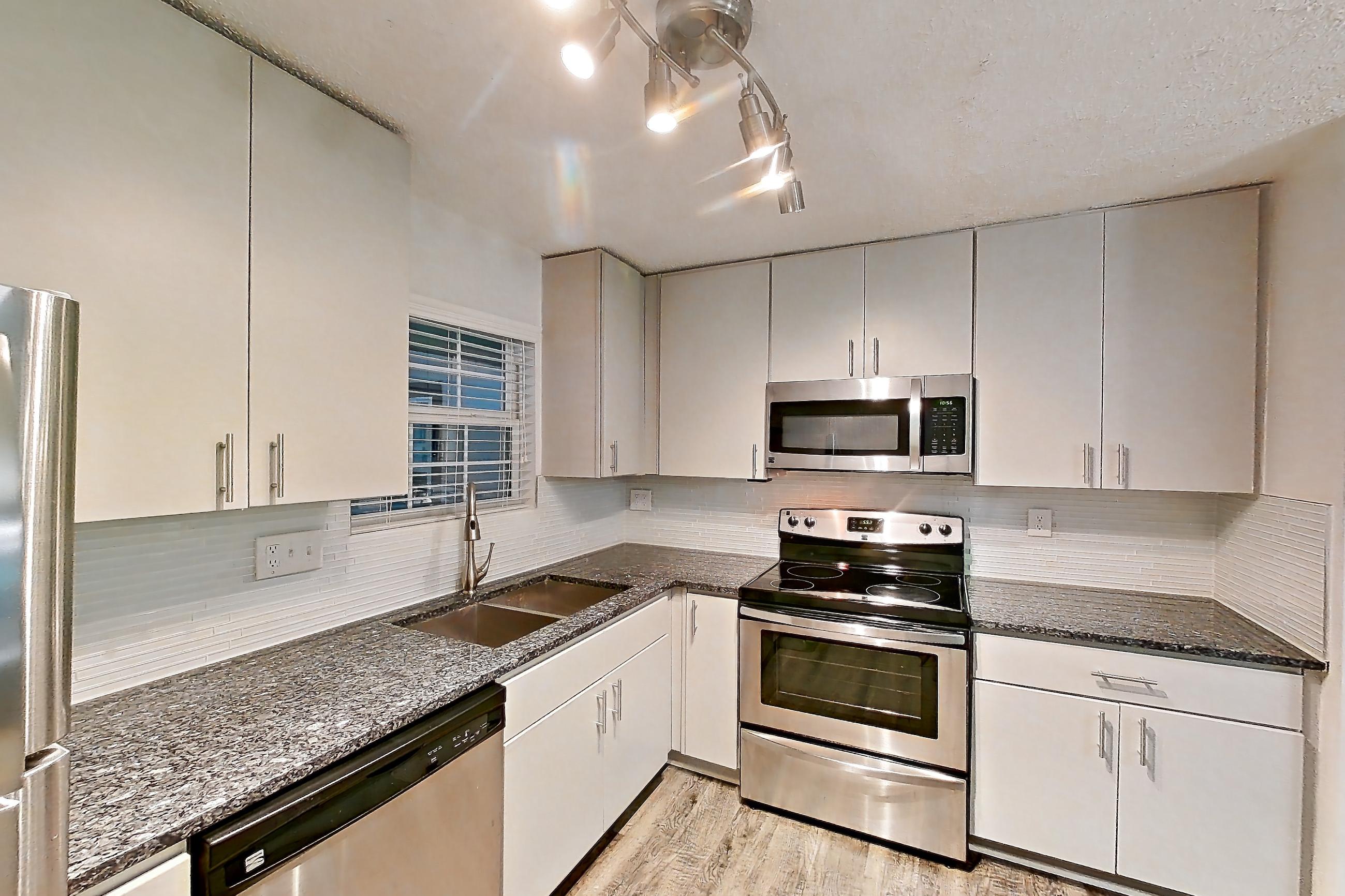 Kitchen with dark stone countertops, dishwasher, electric range, fireplace, light countertops, light wood-finish flooring, microwave, oven/range, refrigerator, stainless steel appliances, and tile fireplace, Apartment 12 at Cortland Cotswold