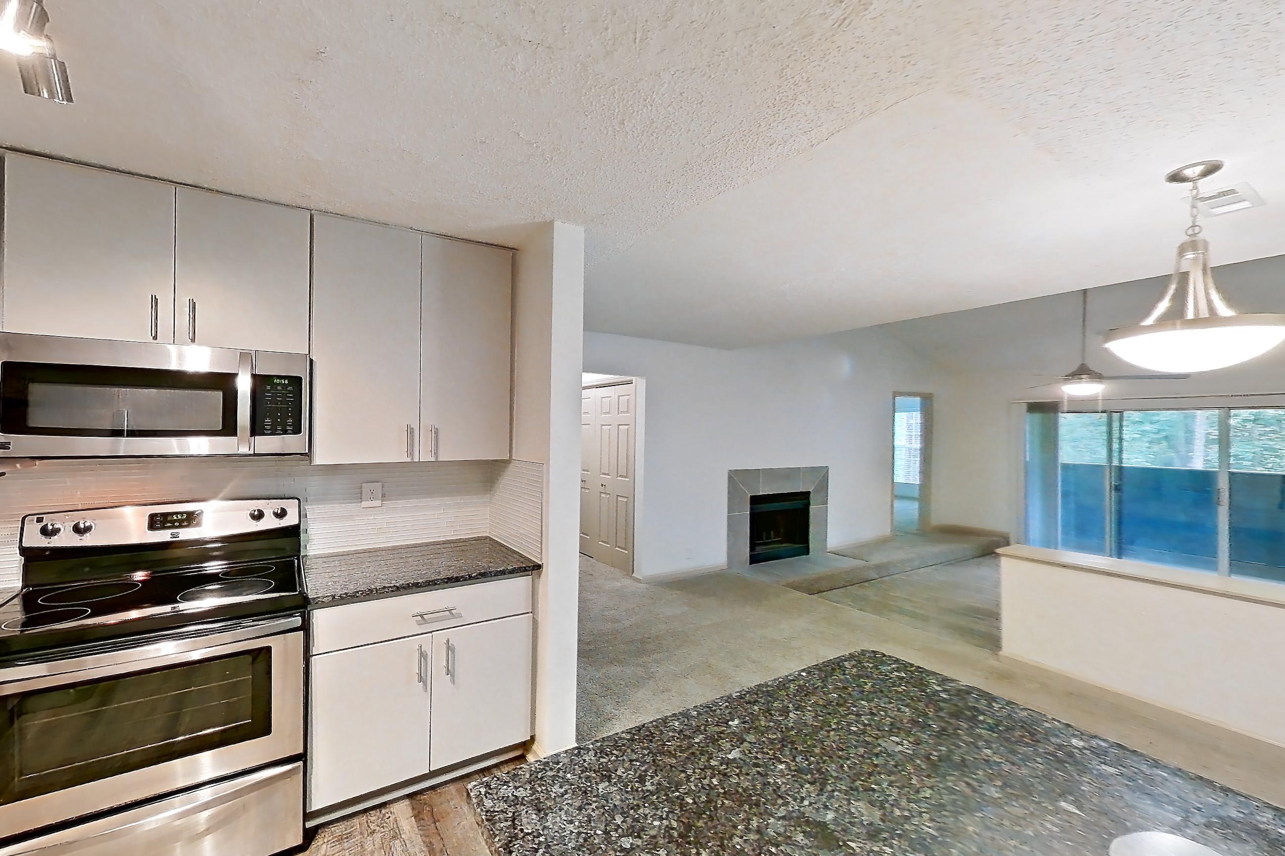 Kitchen with dark stone countertops, dishwasher, electric range, fireplace, light countertops, light wood-finish flooring, microwave, oven/range, refrigerator, stainless steel appliances, and tile fireplace, Apartment 12 at Cortland Cotswold