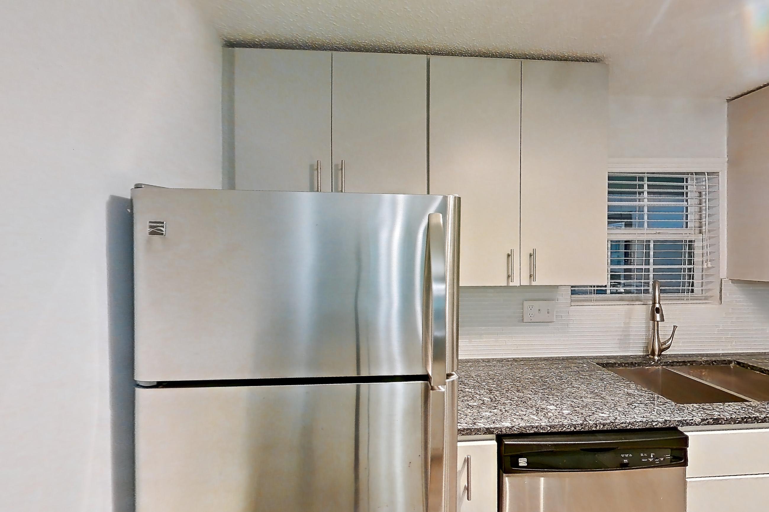 Kitchen with dark stone countertops, dishwasher, electric range, fireplace, light countertops, light wood-finish flooring, microwave, oven/range, refrigerator, stainless steel appliances, and tile fireplace, Apartment 12 at Cortland Cotswold