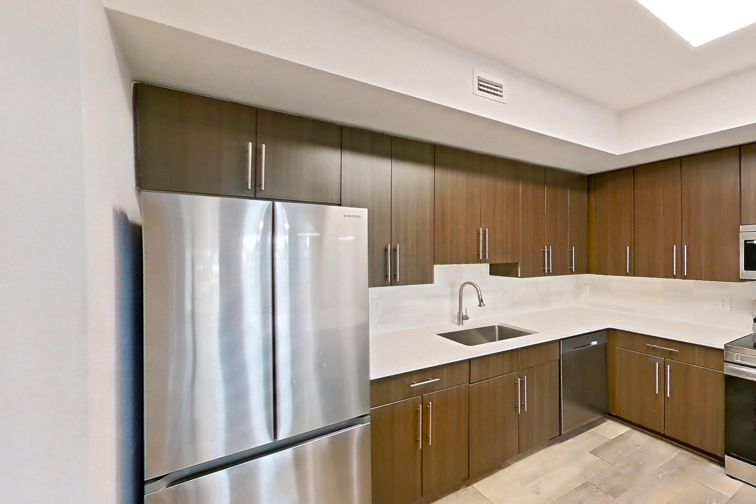 Kitchen entryway with electric range, light countertops, light stone countertops, light wood-finish flooring, oven/range, refrigerator, and stainless steel appliances, Apartment 12-202 at Cortland West Palm