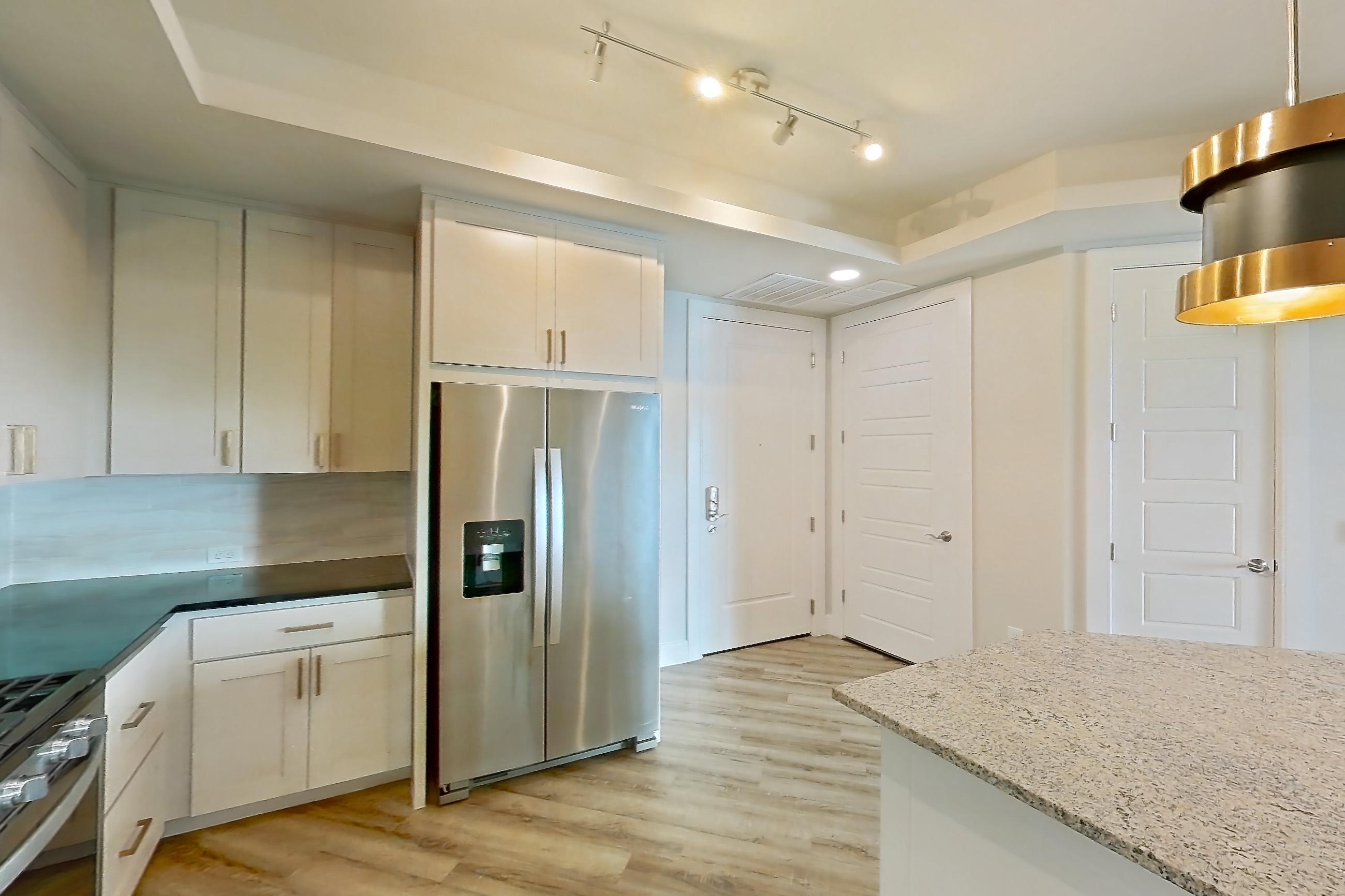 Kitchen with dark stone countertops, dishwasher, gas range, light countertops, light stone countertops, light wood-finish flooring, oven/range, refrigerator, stainless steel appliances, and water & ice dispenser, Apartment 224 at Cortland Biltmore
