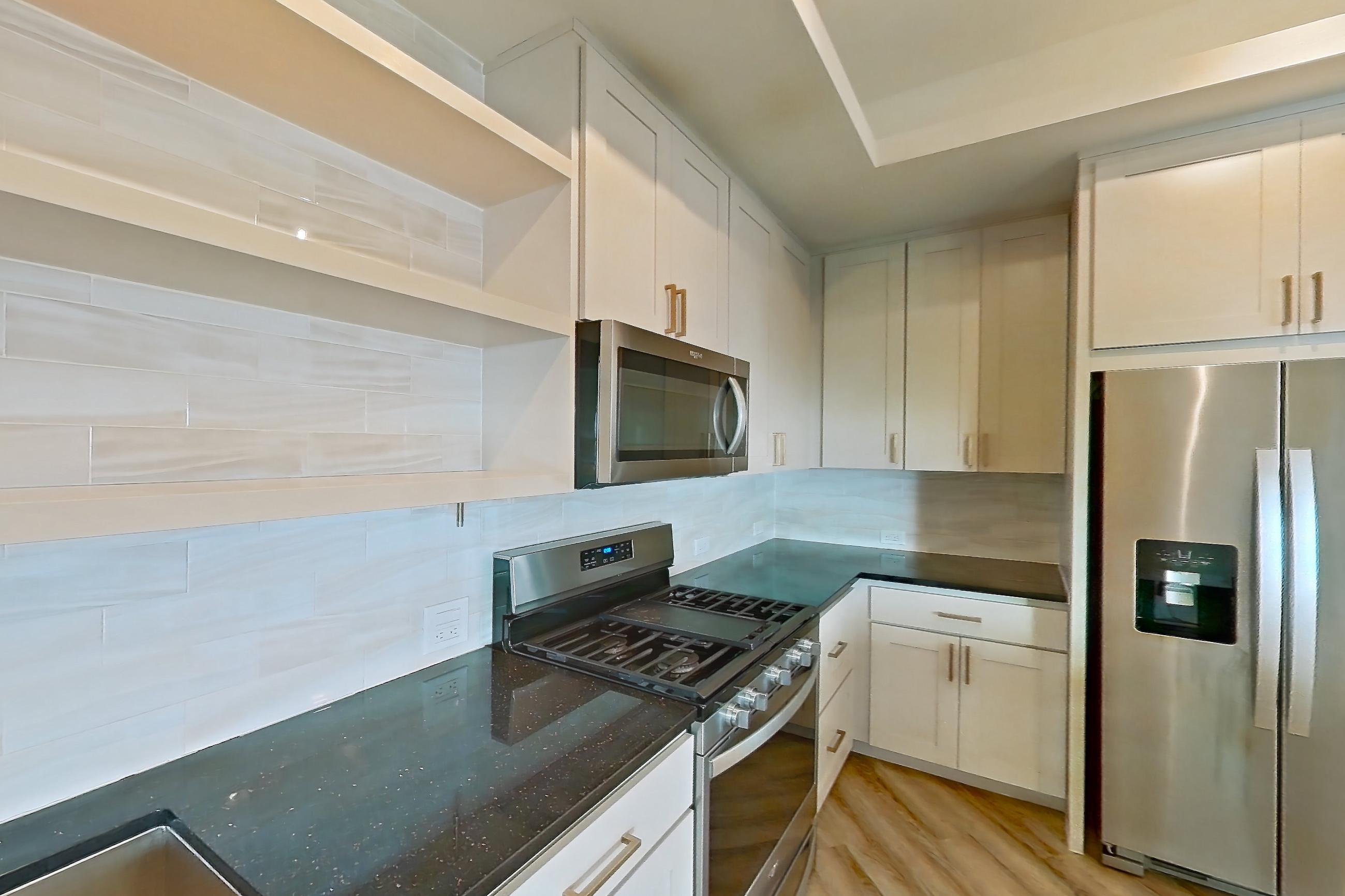 Kitchen with dark stone countertops, dishwasher, gas range, light countertops, light stone countertops, light wood-finish flooring, oven/range, refrigerator, stainless steel appliances, and water & ice dispenser, Apartment 224 at Cortland Biltmore