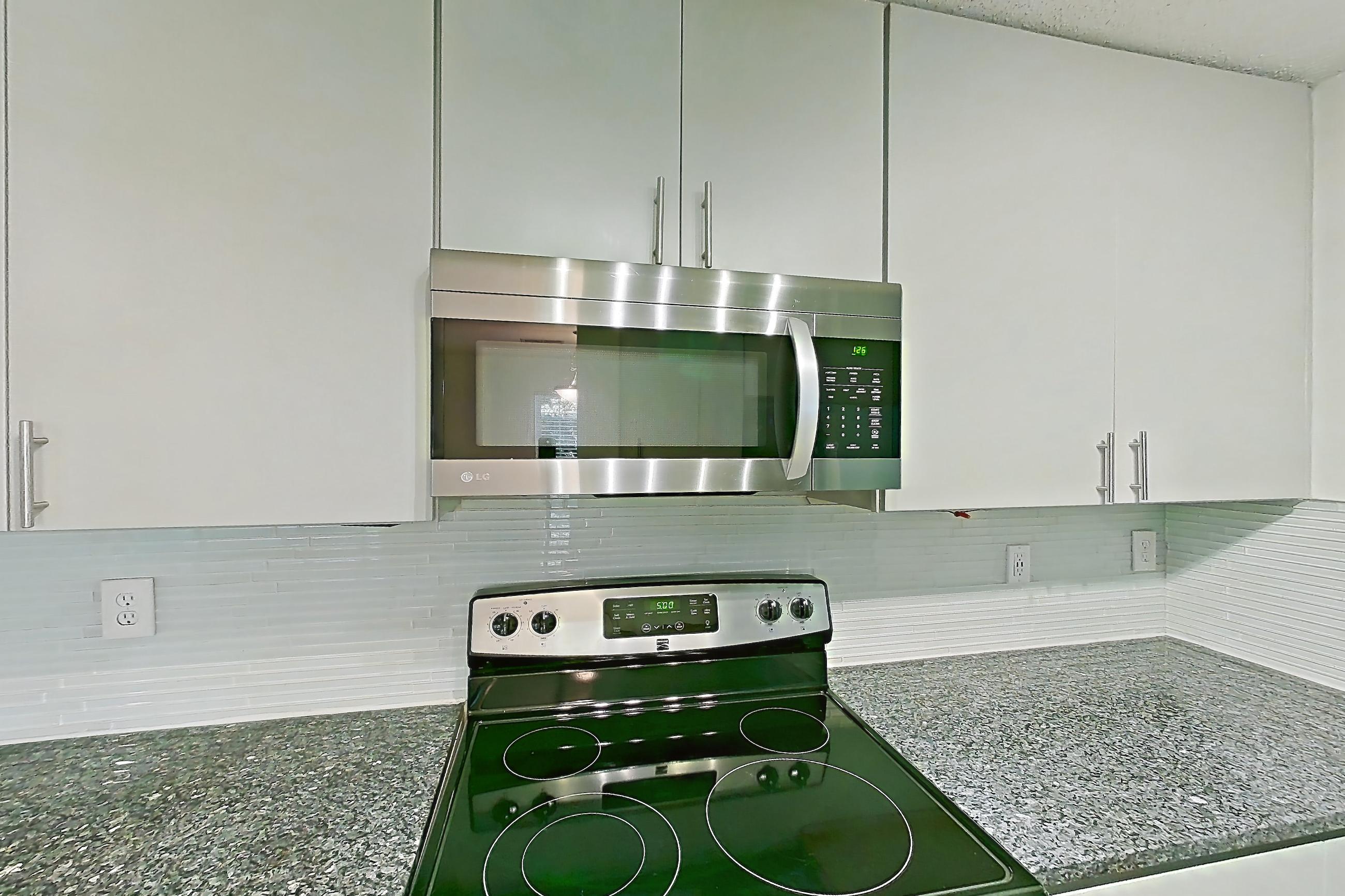 Kitchen with dark stone countertops, dishwasher, electric range, fireplace, light countertops, light stone countertops, light wood-finish flooring, microwave, oven/range, refrigerator, stainless steel appliances, and tile fireplace, Apartment 11 at Cortland Cotswold