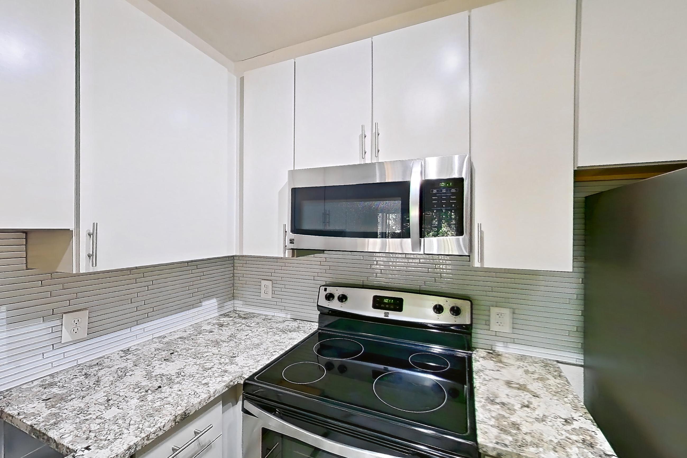 Kitchen with dishwasher, electric range, light countertops, light stone countertops, light wood-finish flooring, microwave, oven/range, refrigerator, and stainless steel appliances, Apartment 0823 at Cortland Seventy Seven