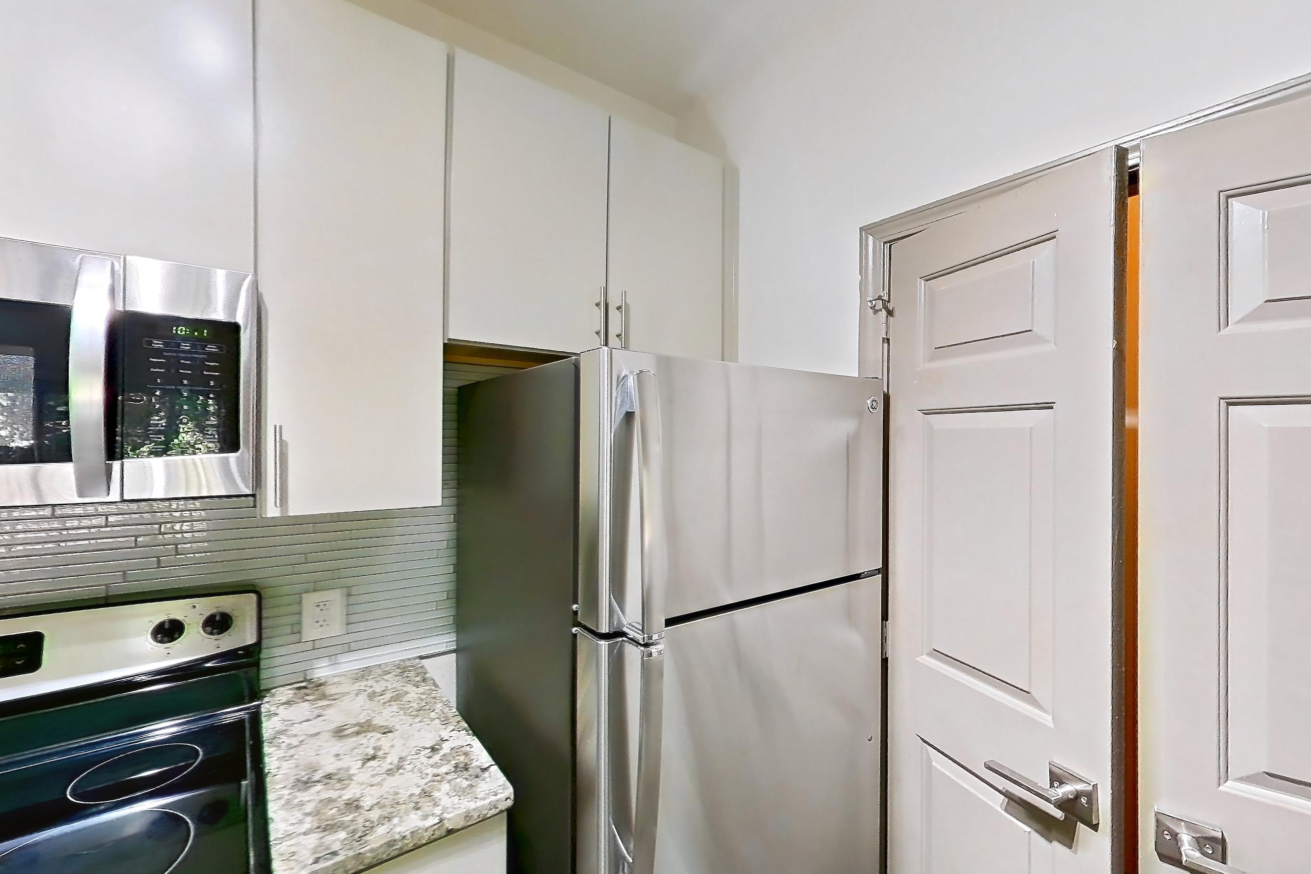 Kitchen with dishwasher, electric range, light countertops, light stone countertops, light wood-finish flooring, microwave, oven/range, refrigerator, and stainless steel appliances, Apartment 0823 at Cortland Seventy Seven