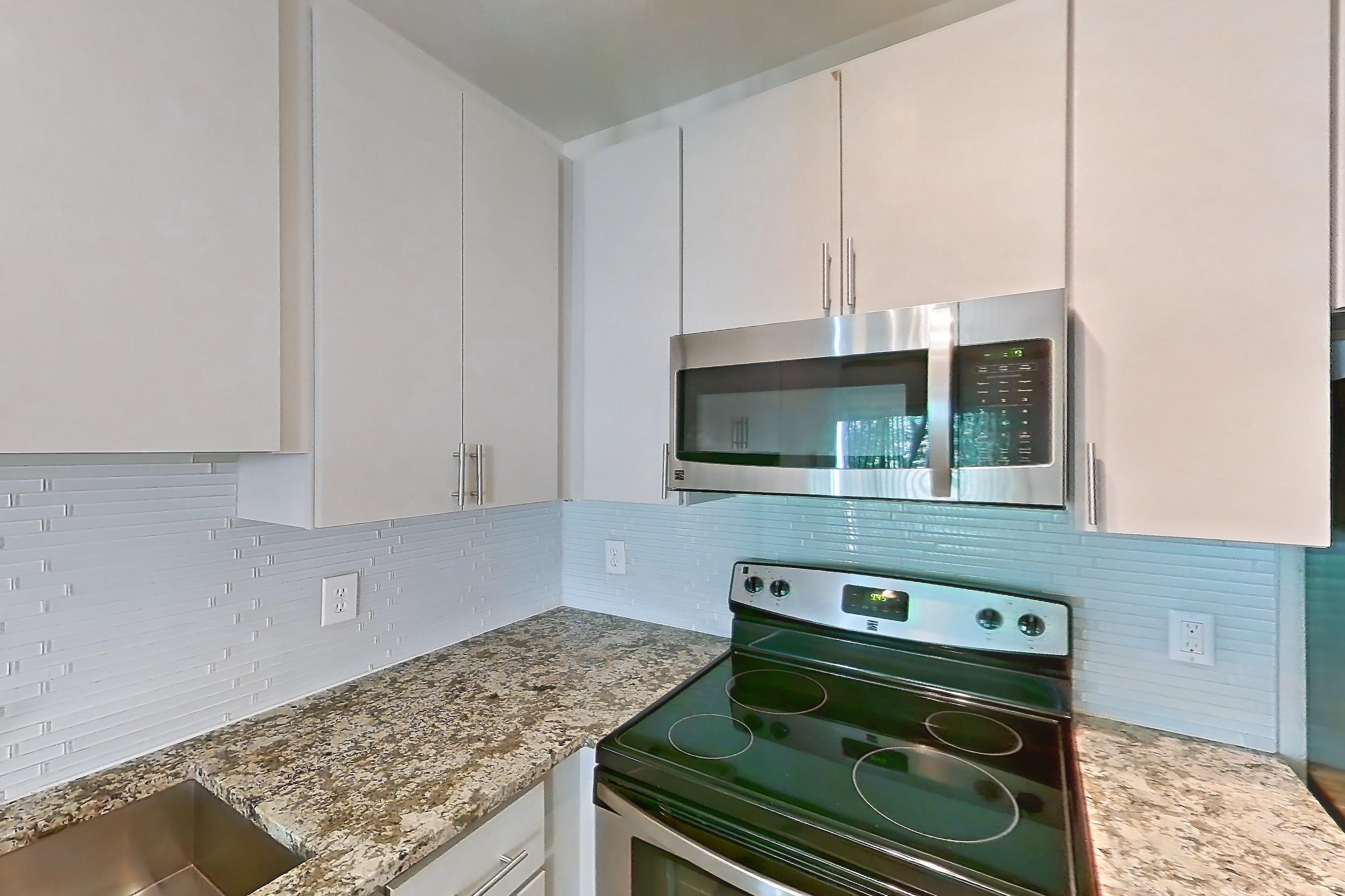 Kitchen with black appliances, dishwasher, electric range, light countertops, light stone countertops, light wood-finish flooring, microwave, oven/range, refrigerator, and stainless steel appliances, Apartment 0833 at Cortland Seventy Seven
