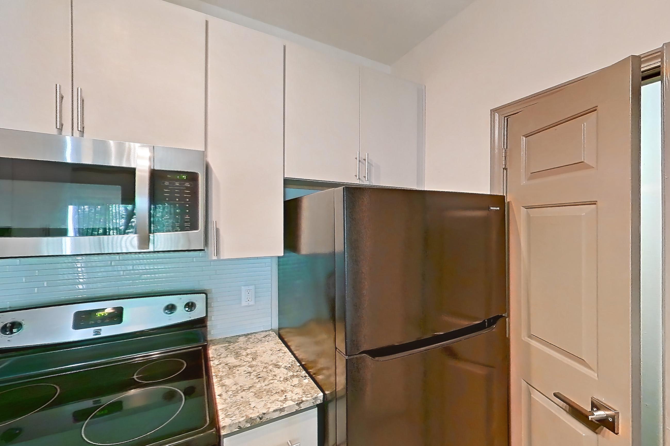Kitchen with black appliances, dishwasher, electric range, light countertops, light stone countertops, light wood-finish flooring, microwave, oven/range, refrigerator, and stainless steel appliances, Apartment 0833 at Cortland Seventy Seven