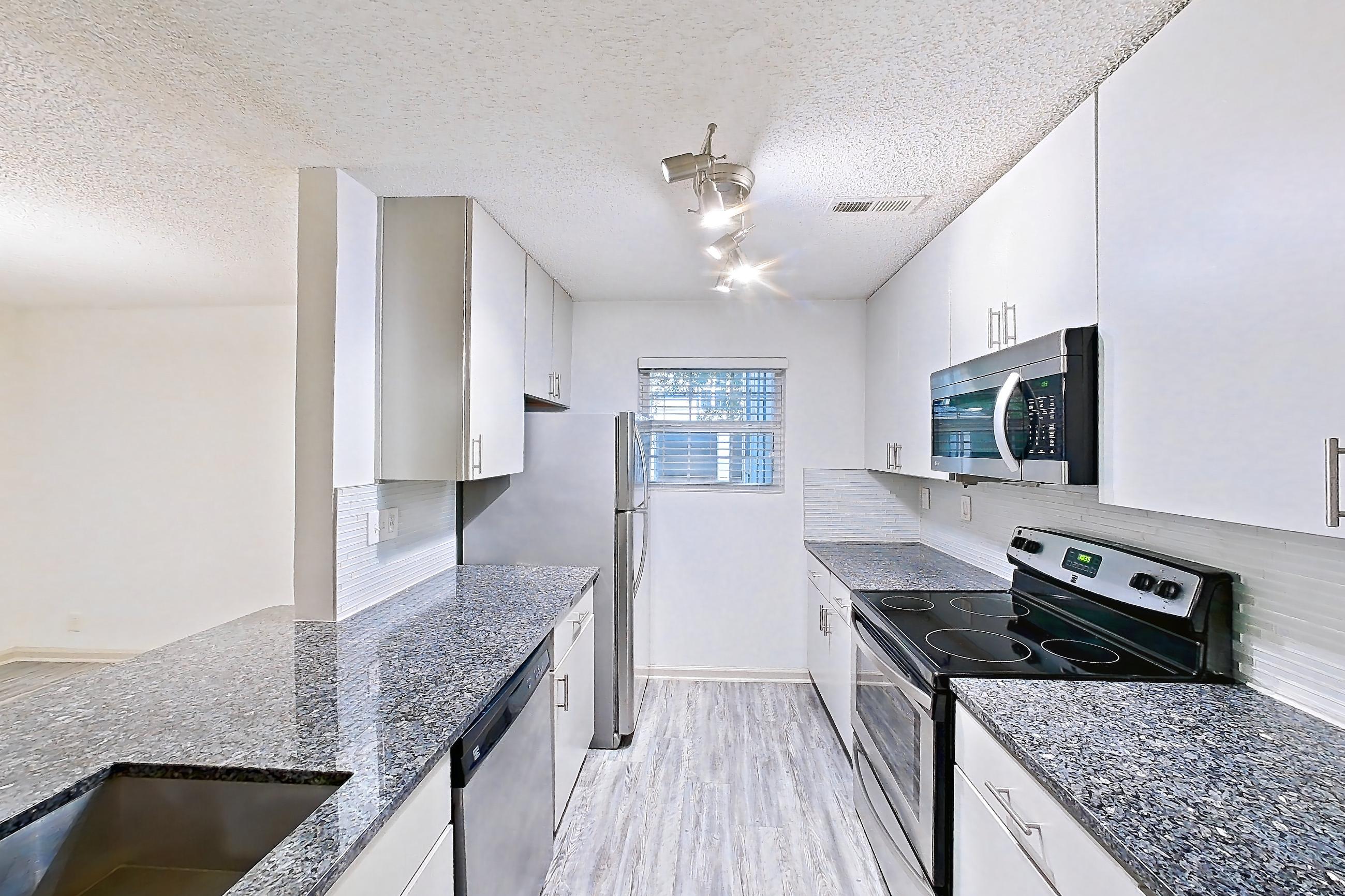 Kitchen with black appliances, dark stone countertops, dark wood-finish flooring, dishwasher, electric range, fireplace, light countertops, light wood-finish flooring, microwave, oven/range, refrigerator, and stainless steel appliances, Apartment 4 at Cortland Cotswold