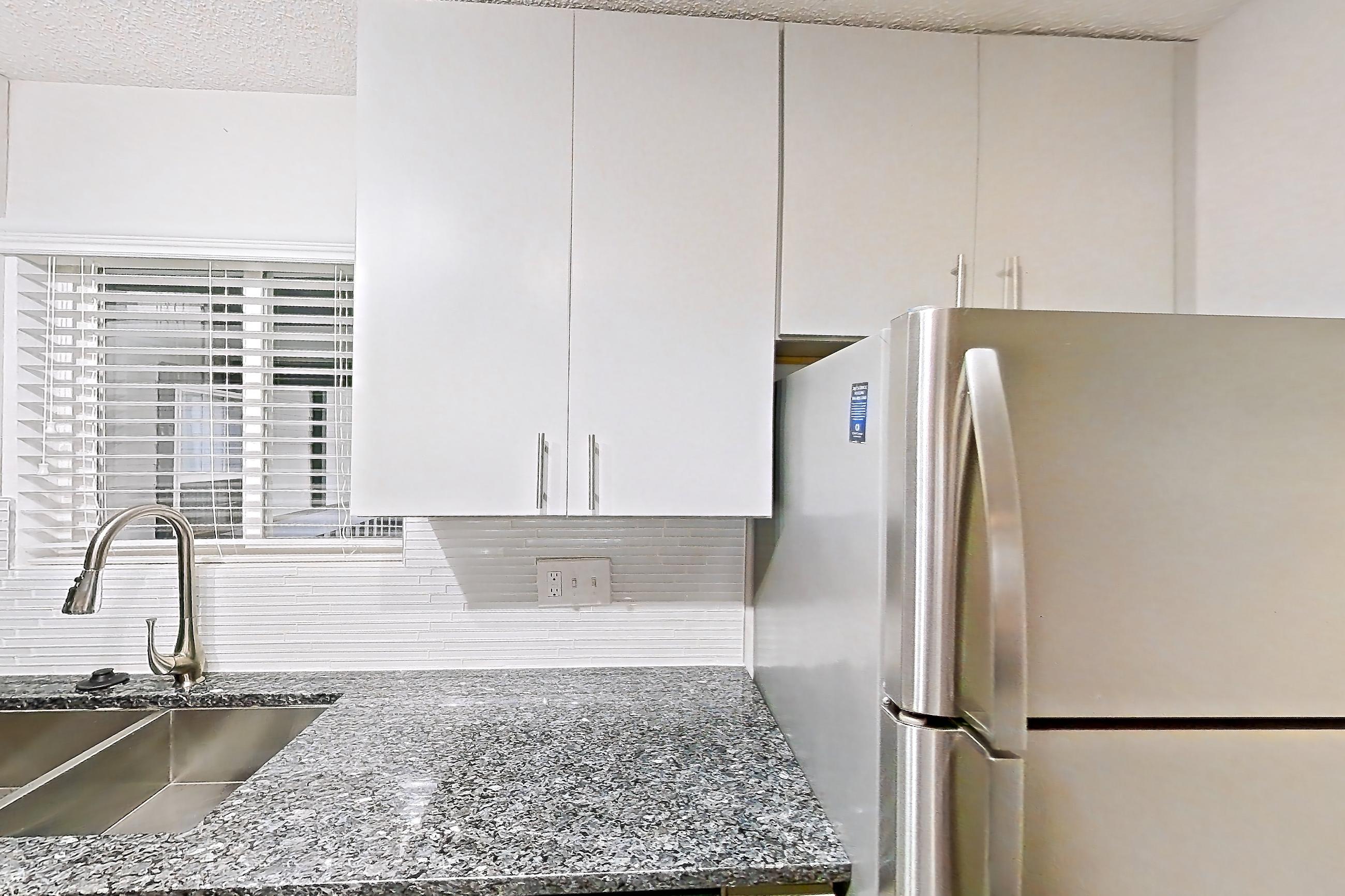 Kitchen with dark stone countertops, dishwasher, electric range, fireplace, light carpet, light countertops, light wood-finish flooring, oven/range, refrigerator, stainless steel appliances, and tile fireplace, Apartment 9 at Cortland Cotswold