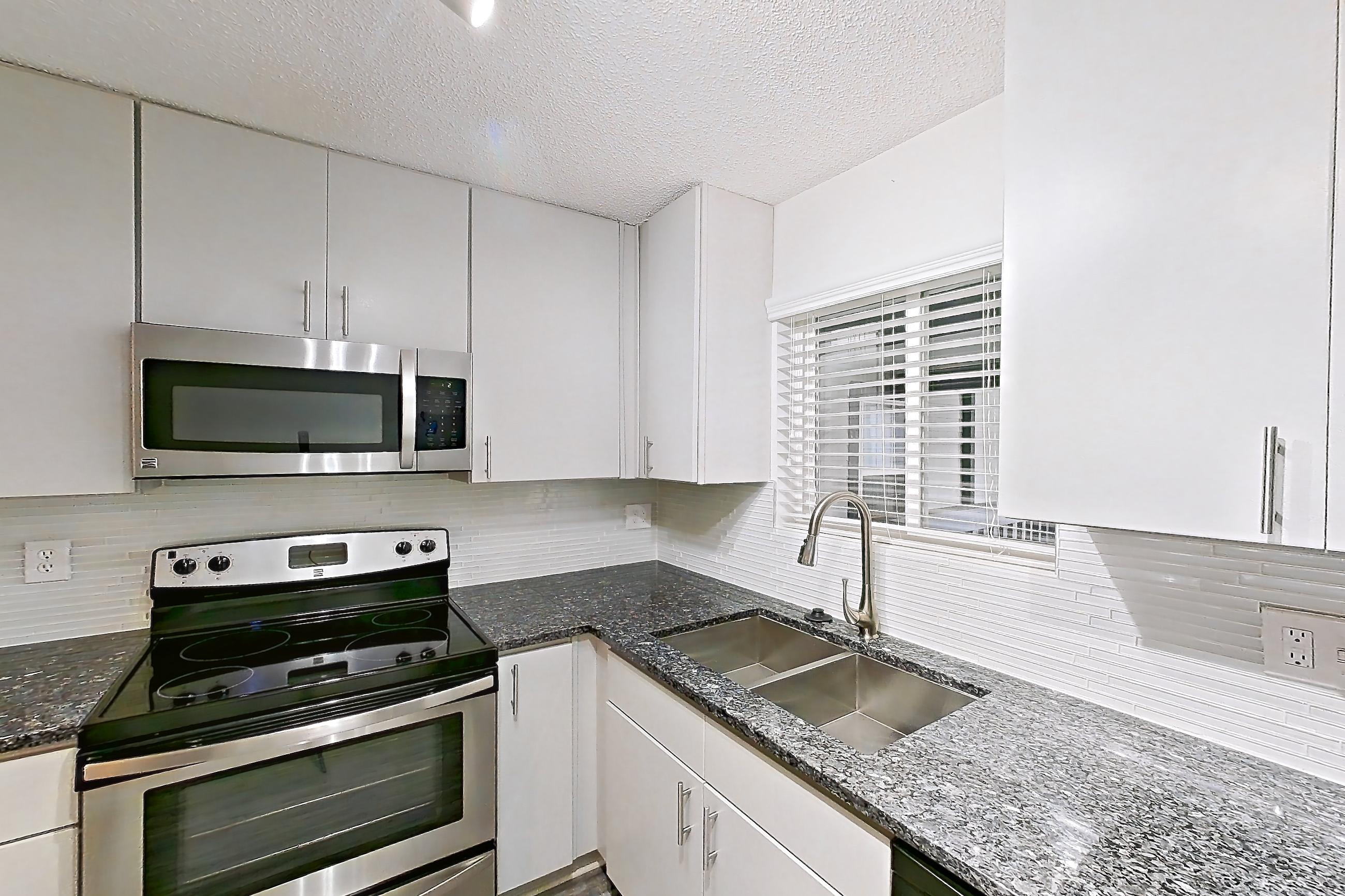Kitchen with dark stone countertops, dishwasher, electric range, fireplace, light carpet, light countertops, light wood-finish flooring, oven/range, refrigerator, stainless steel appliances, and tile fireplace, Apartment 9 at Cortland Cotswold