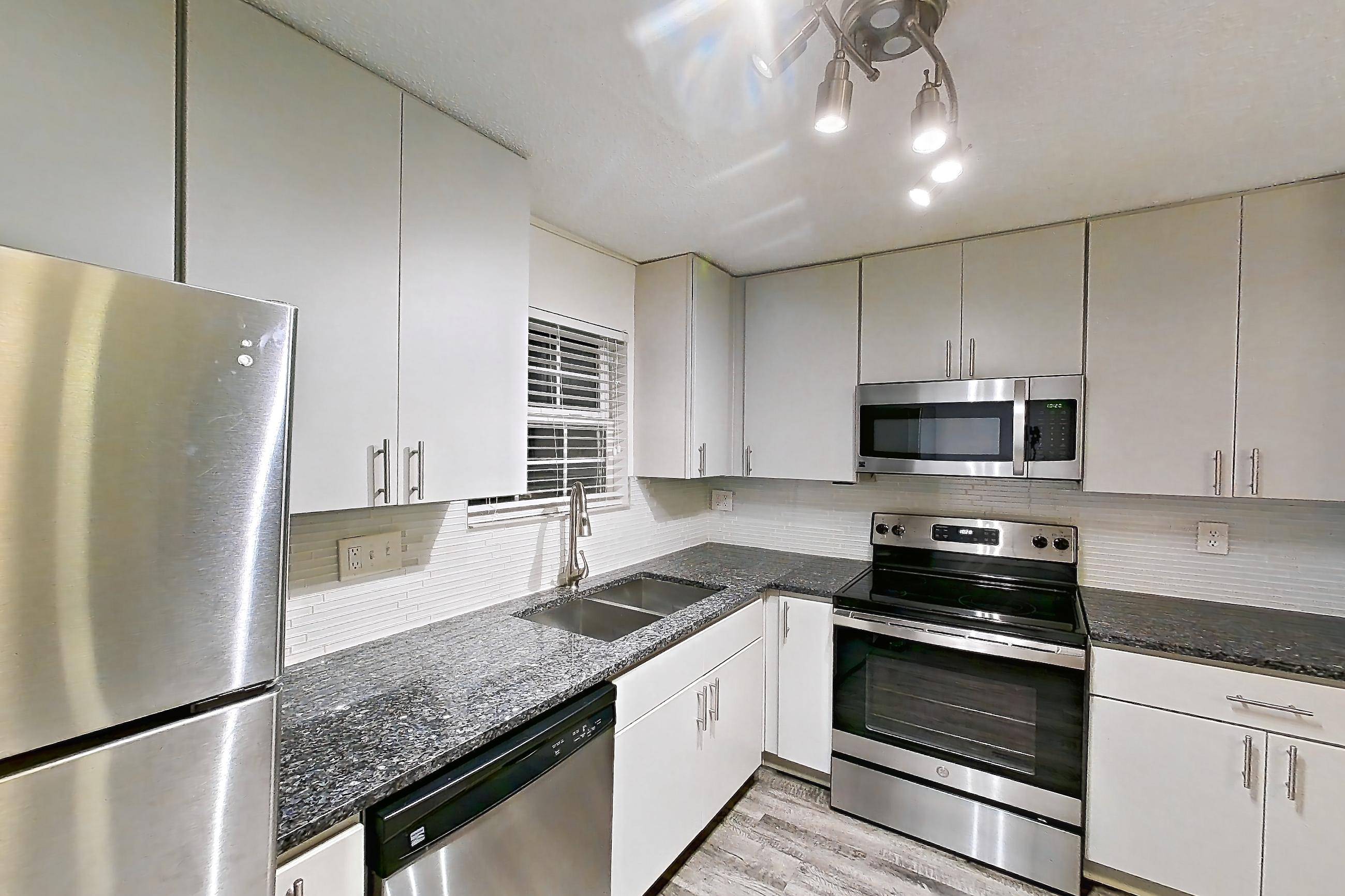 Kitchen with dark stone countertops, dishwasher, electric range, fireplace, light countertops, light wood-finish flooring, microwave, oven/range, refrigerator, stainless steel appliances, and tile fireplace, Apartment 2 at Cortland Cotswold