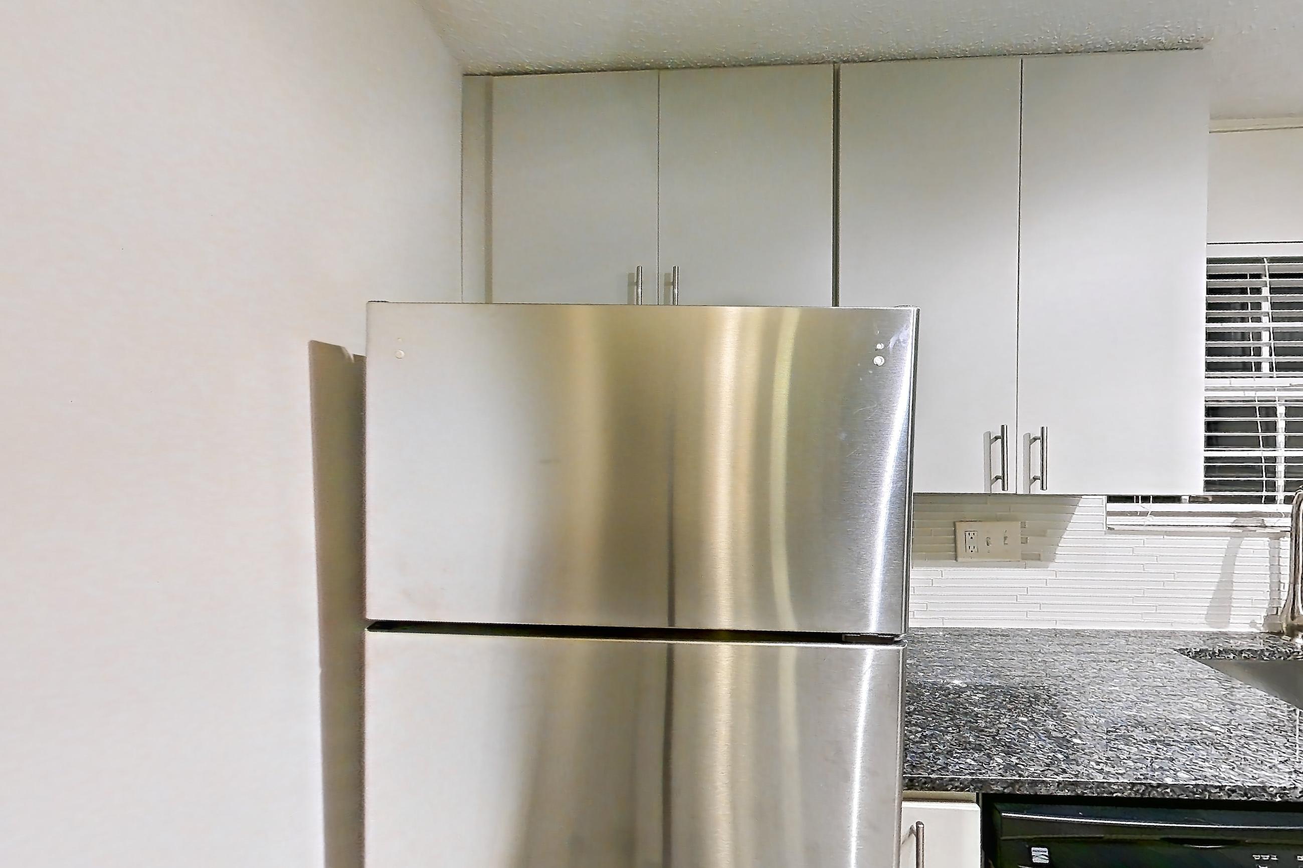 Kitchen with dark stone countertops, dishwasher, electric range, fireplace, light countertops, light wood-finish flooring, microwave, oven/range, refrigerator, stainless steel appliances, and tile fireplace, Apartment 2 at Cortland Cotswold