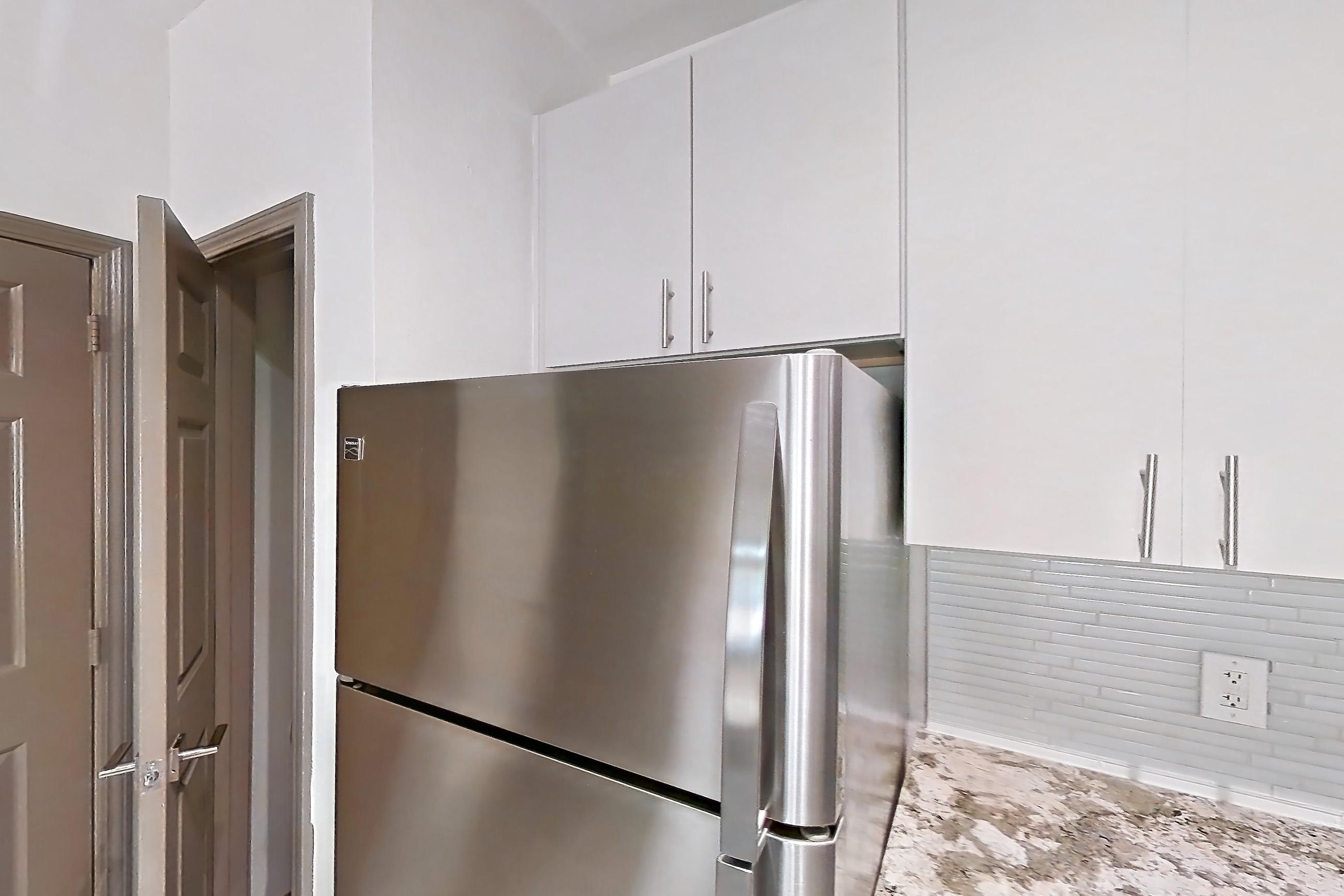 Kitchen with dishwasher, electric range, kitchen island, light countertops, light stone countertops, light wood-finish flooring, microwave, oven/range, refrigerator, and stainless steel appliances, Apartment 1317 at Cortland Seventy Seven