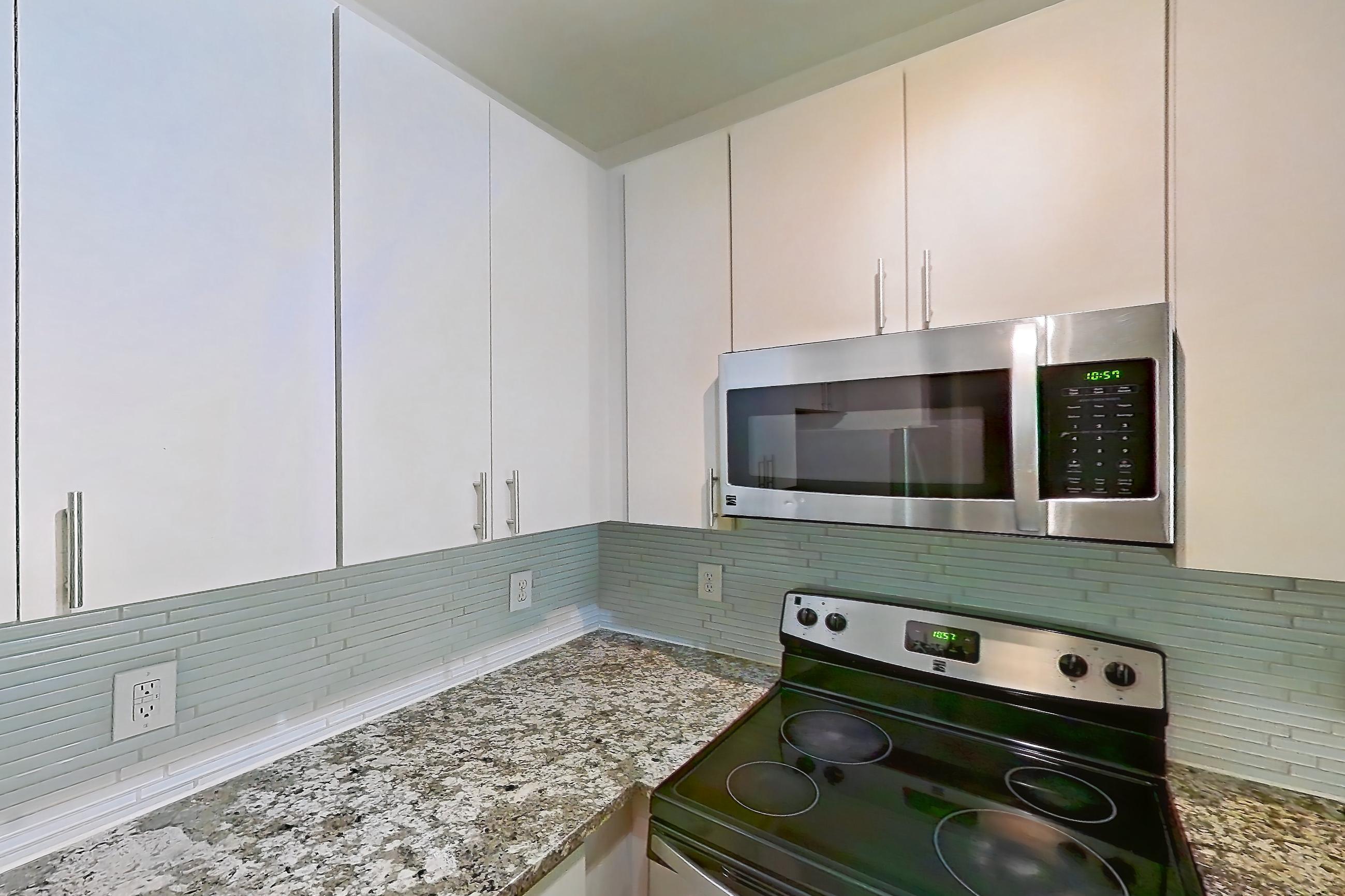 Kitchen with dishwasher, electric range, light countertops, light stone countertops, light wood-finish flooring, microwave, oven/range, and stainless steel appliances, Apartment 1337 at Cortland Seventy Seven