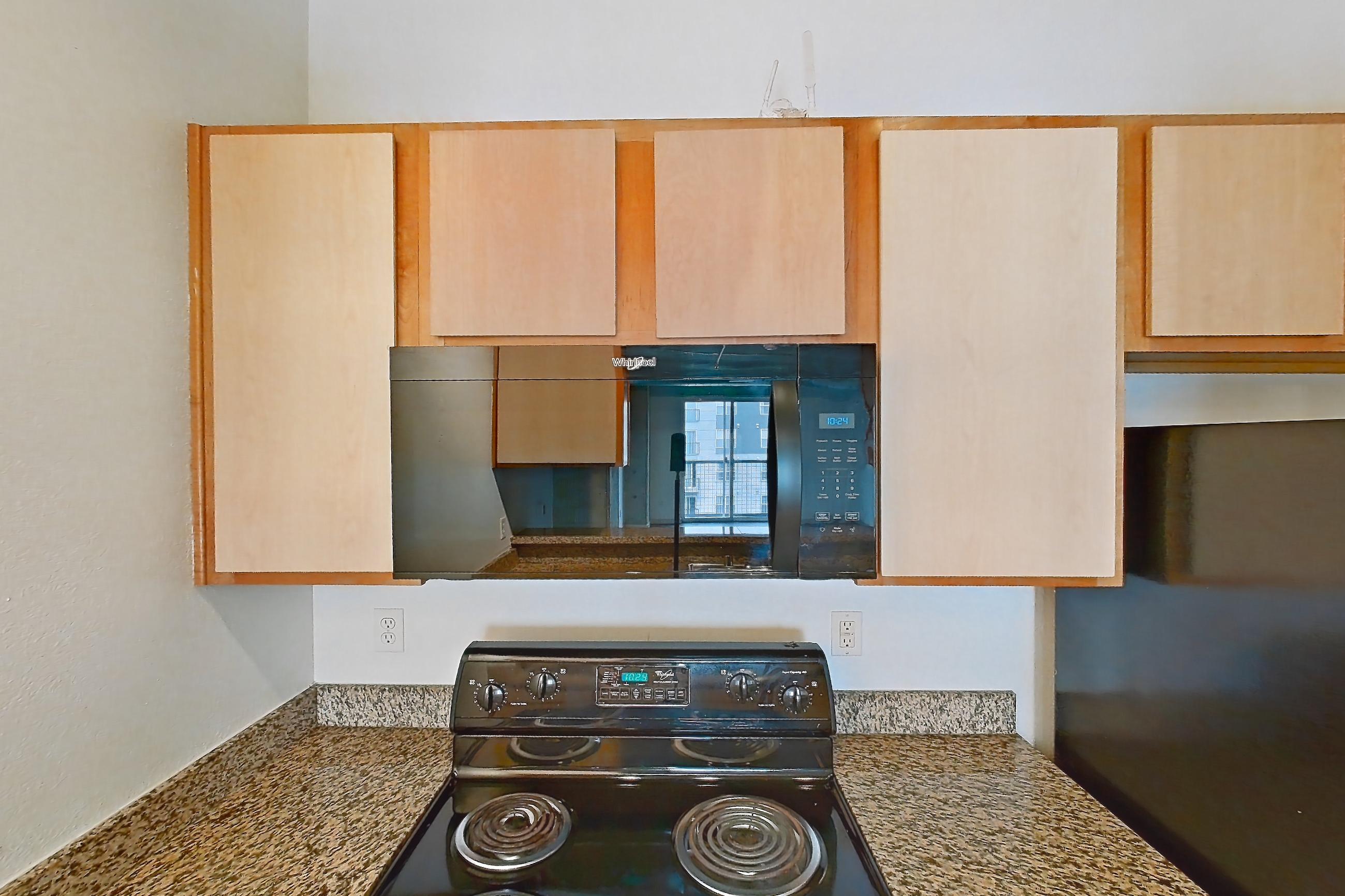 Kitchen with black appliances, dark stone countertops, dark wood-finish flooring, dishwasher, electric range, light stone countertops, light wood-finish flooring, microwave, oven/range, and refrigerator, Apartment 1439 at Cortland on Blake