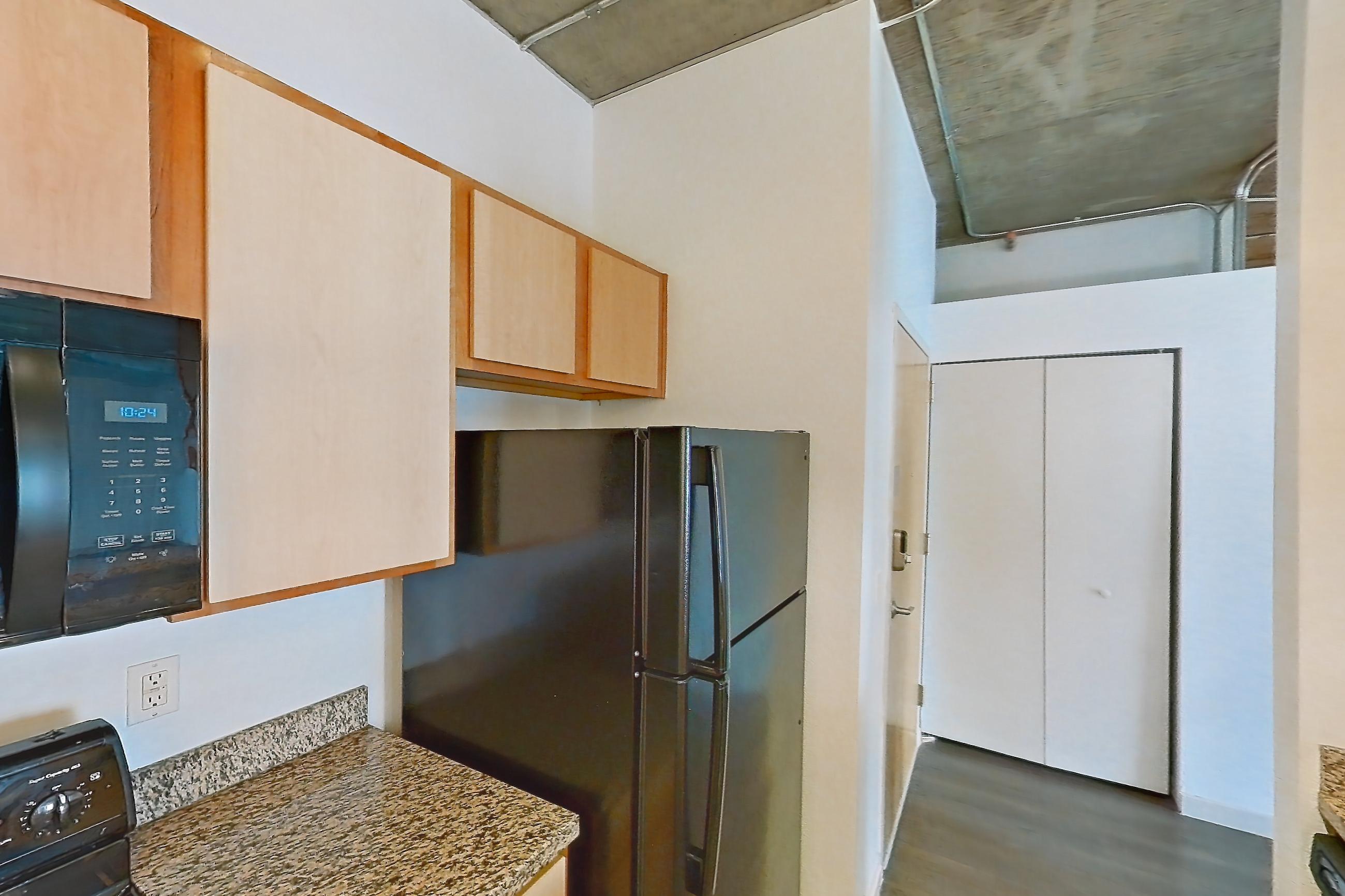 Kitchen with black appliances, dark stone countertops, dark wood-finish flooring, dishwasher, electric range, light stone countertops, light wood-finish flooring, microwave, oven/range, and refrigerator, Apartment 1439 at Cortland on Blake